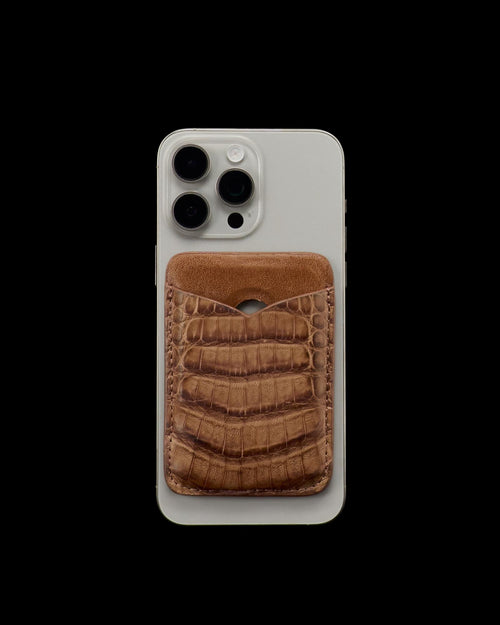 Silver smartphone with a brown, crocodile-patterned leather card holder attached to its back, photographed against a plain white background.