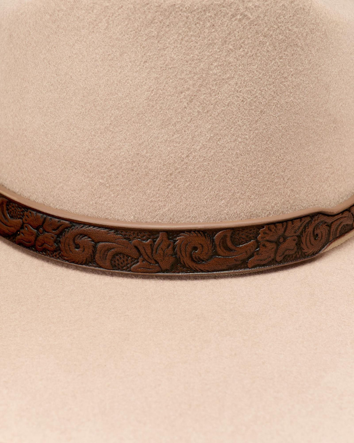 Close-up of a beige felt hat with a brown leather hatband featuring an embossed floral pattern.