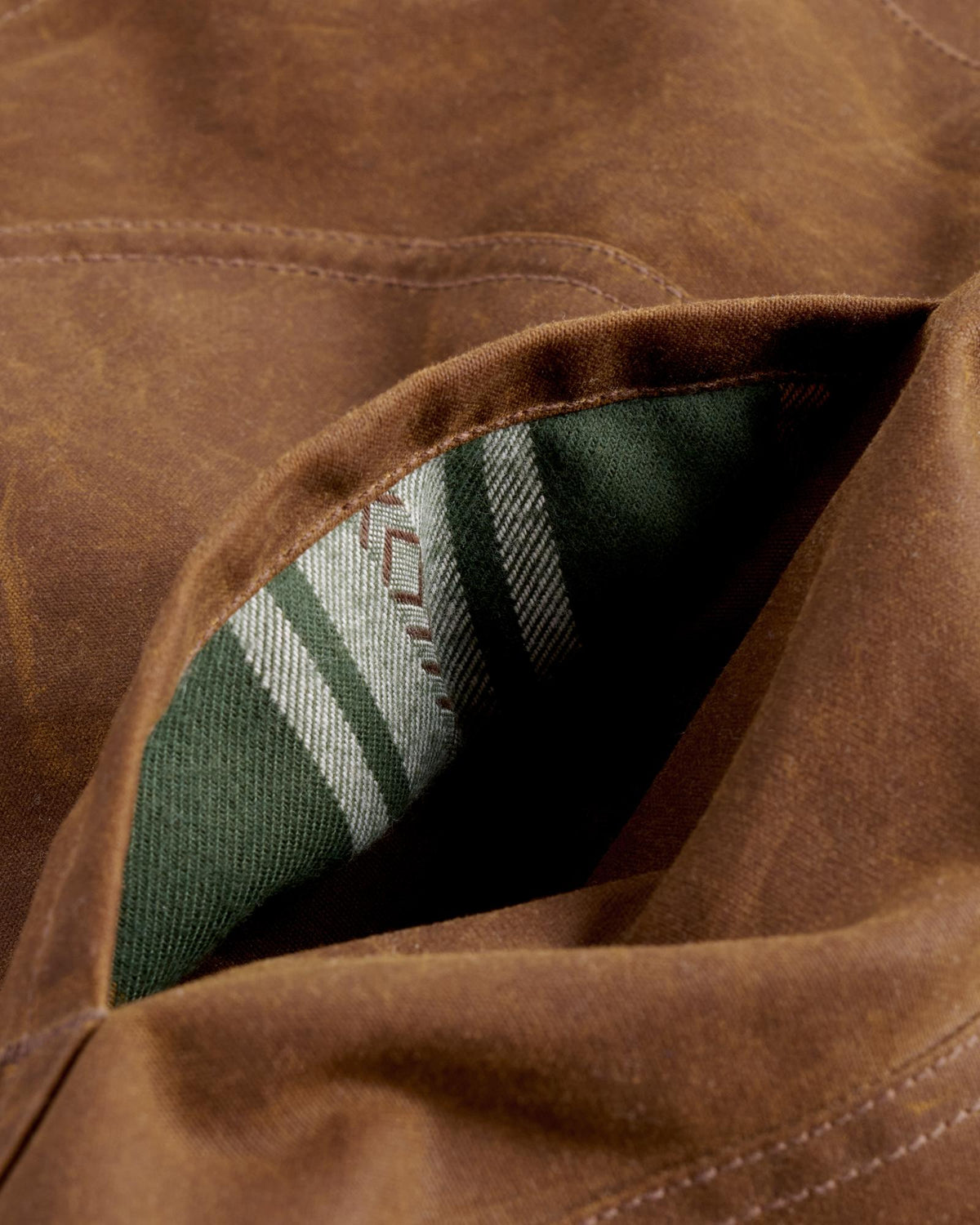 Close-up of a brown waxed canvas pocket with a green and white striped interior lining.