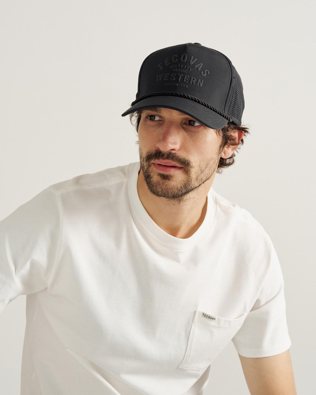A man with a beard wears a black cap with "Tecovas Quality Made Western" text 