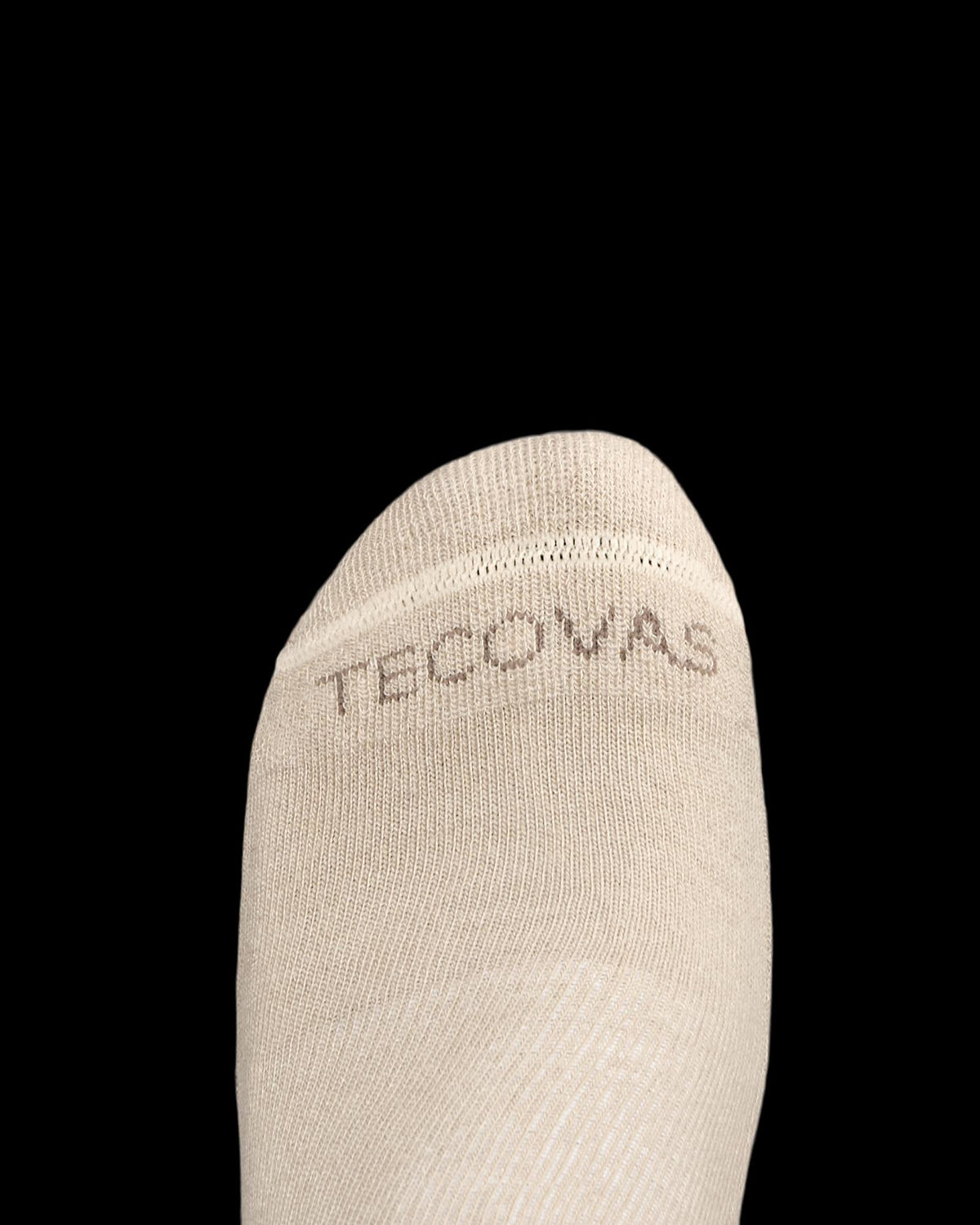 Close-up of the toe of a beige sock with the word "TECOVAS" stitched in brown letters near the seam, shown on a white background.