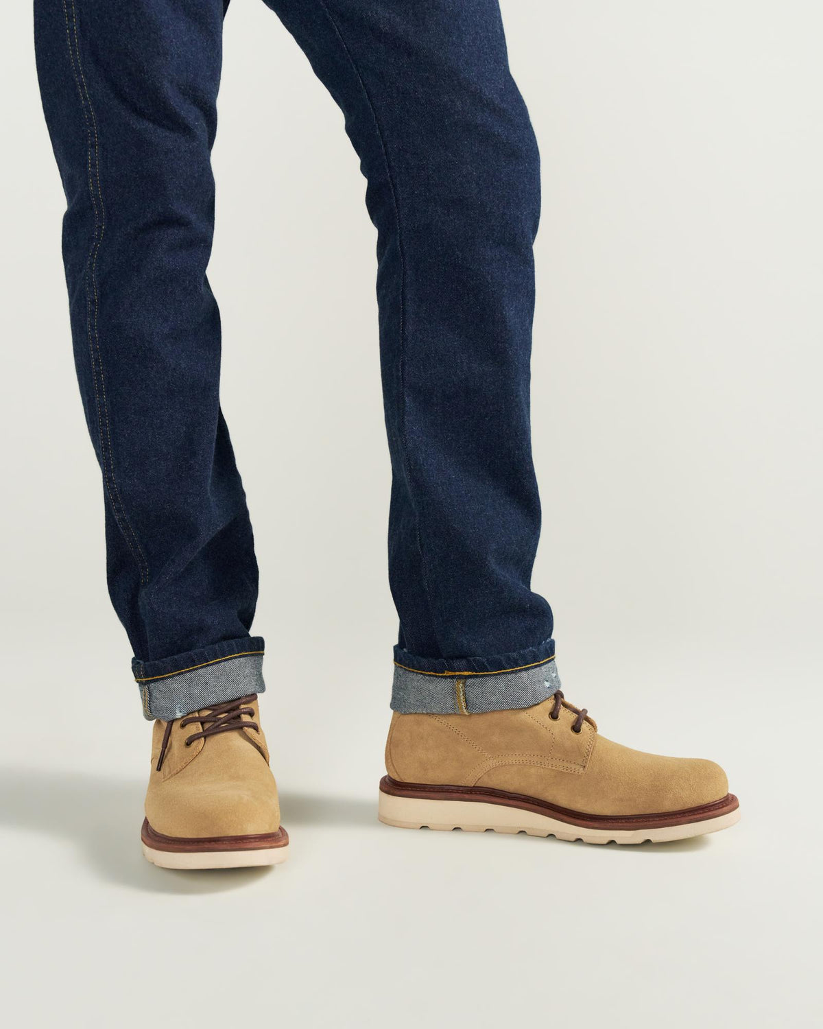 Person wearing dark blue cuffed jeans and The Knox Lace Up Shearling Roughout in Sandstone Roughout, standing on a light-colored surface.