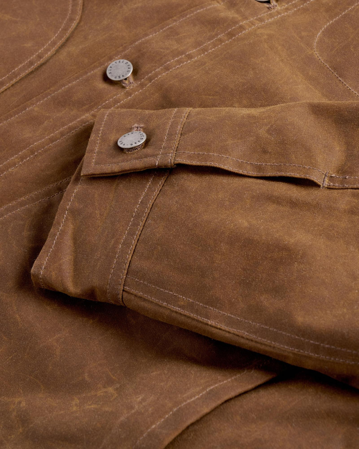 Close-up of a brown waxed canvas jacket sleeve with a branded metal button.