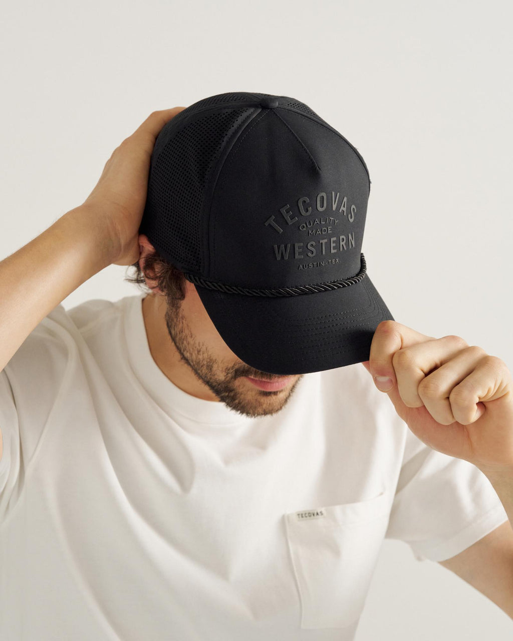 A man with a beard wears a black cap with "Tecovas Quality Made Western" text 