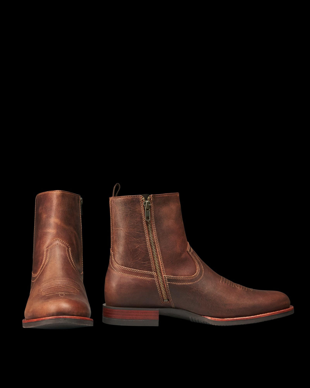 The Wayne in Maplewood Cowhide. Pair of brown cowhide leather ankle boots with side zippers, worn finish, round toes, and low maplewood heels. One boot is shown from the front, the other from the side.