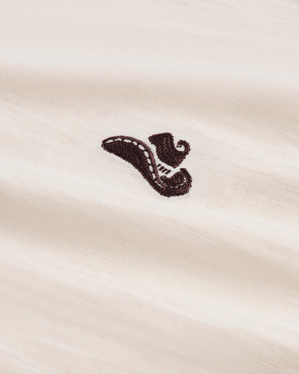 Close-up of a cream-colored fabric with a small, black embroidered design resembling a stylized shoe or horn in the center.