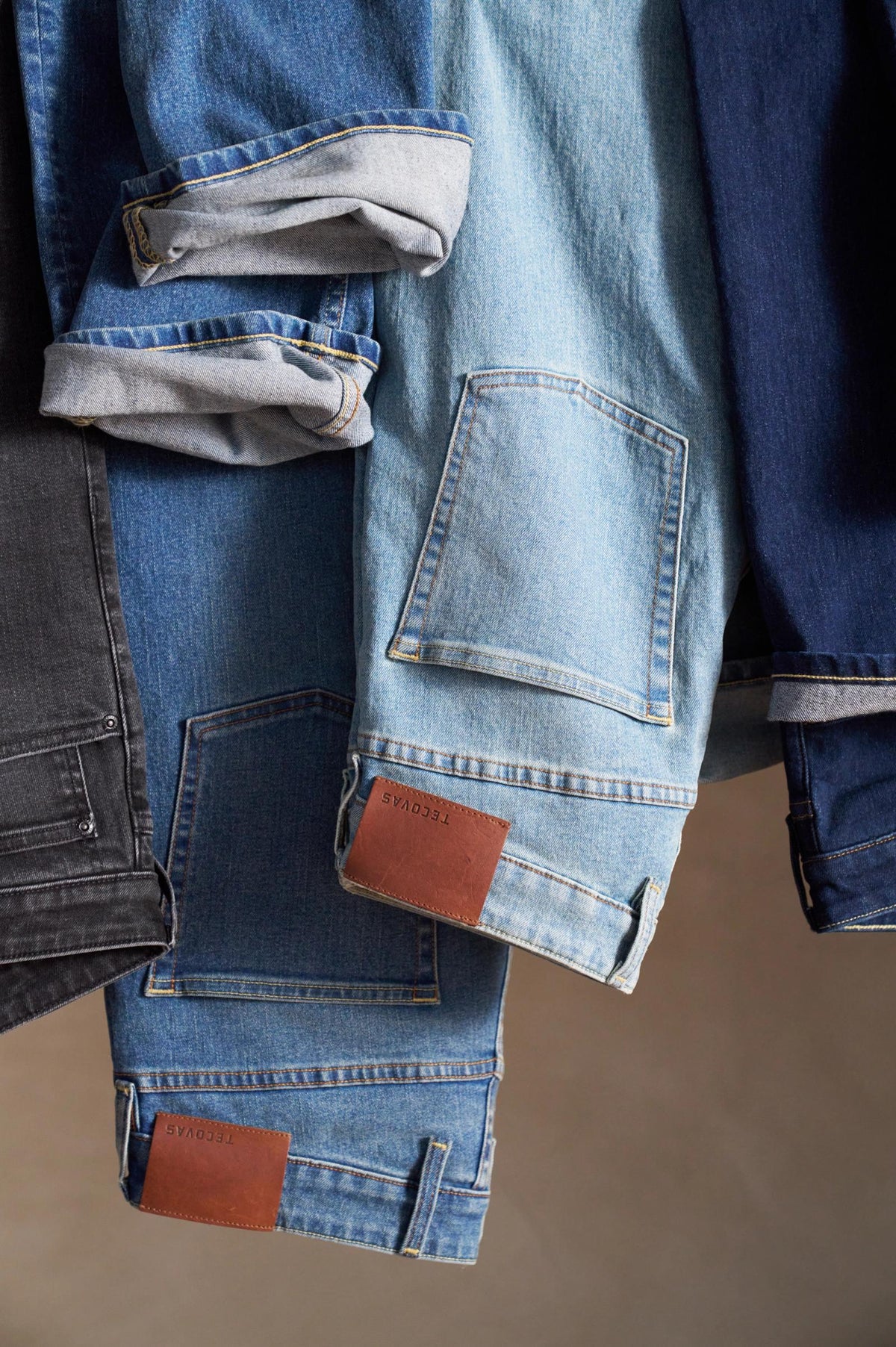 Three denim jackets in black, light blue, and dark blue hang side by side with sleeves rolled up and brown leather patches visible near the hems.