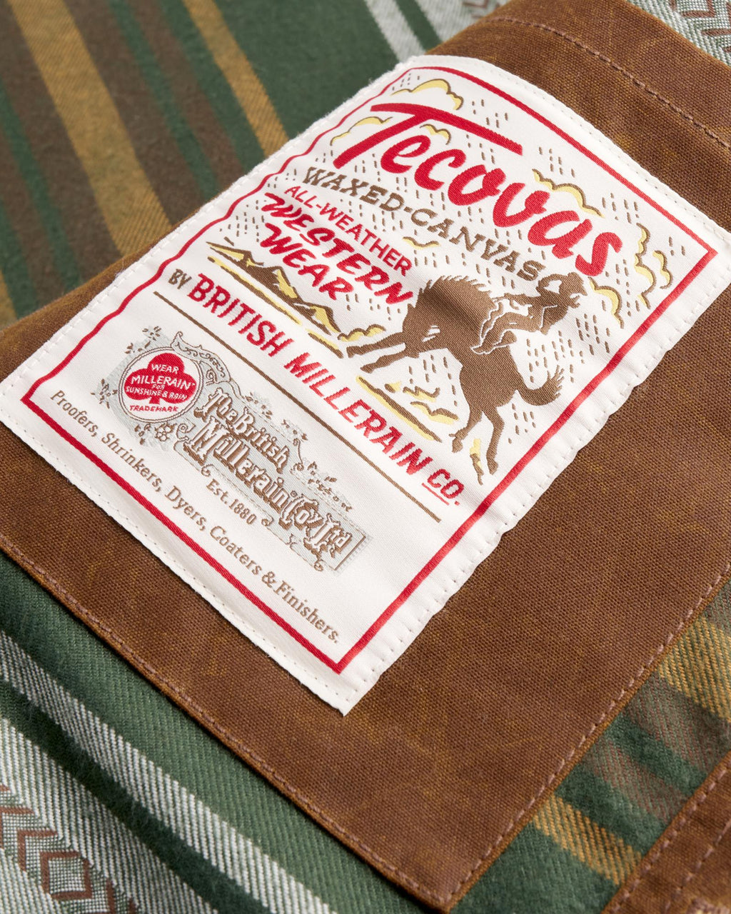 A Tecovas brand patch sewn onto a waxed canvas garment, featuring a bucking bronco illustration and British Millerain Co. text.