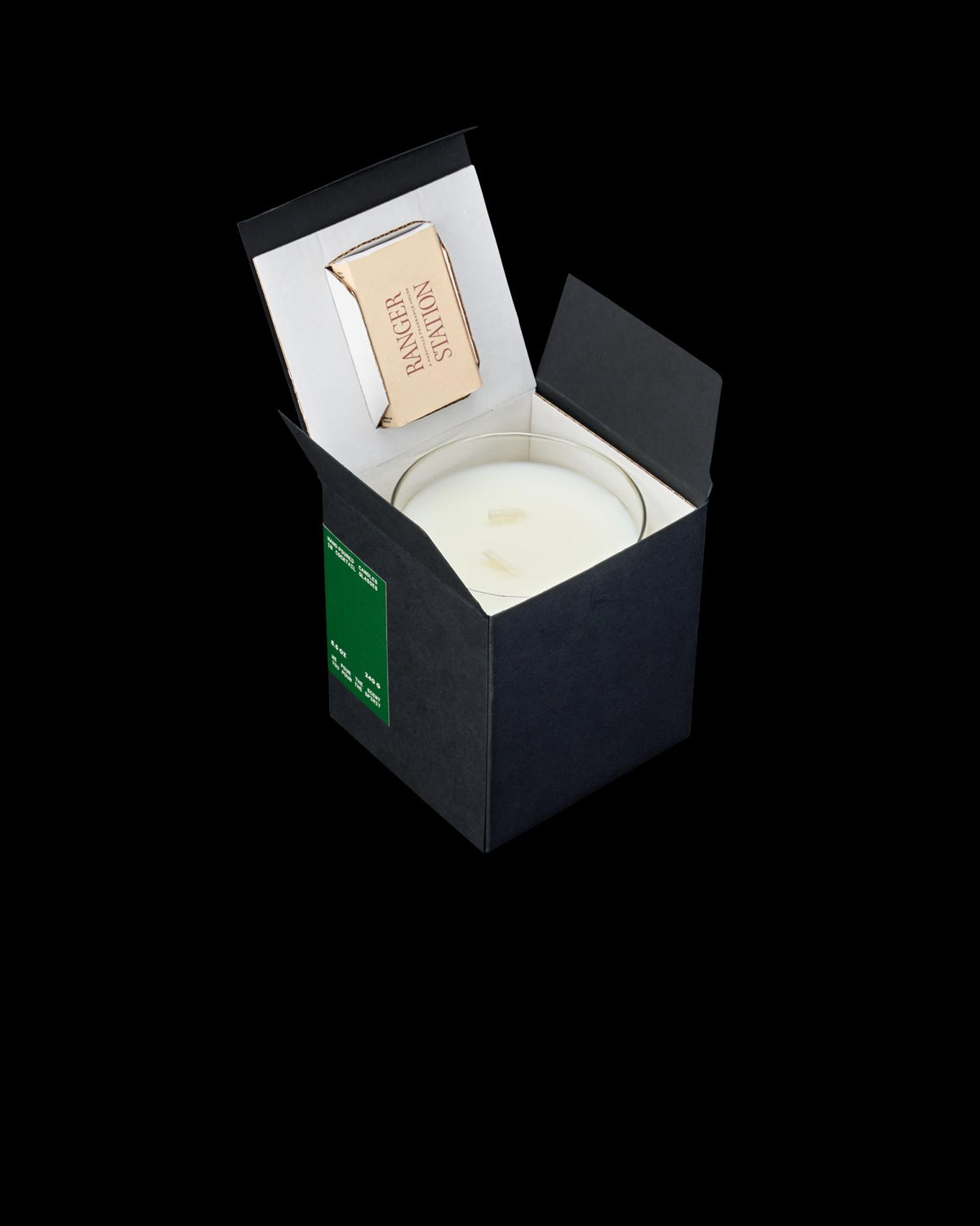 A black candle box is open, revealing a white candle and a small matchbox inside.