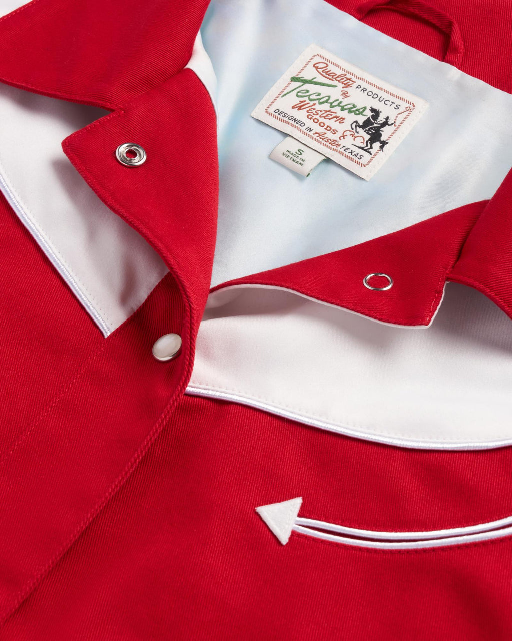 Close-up of a red and white western-style shirt with pearl snap buttons, a pointed pocket detail, and a visible label reading "Ranch Wear" by Rockmount Ranch Wear.