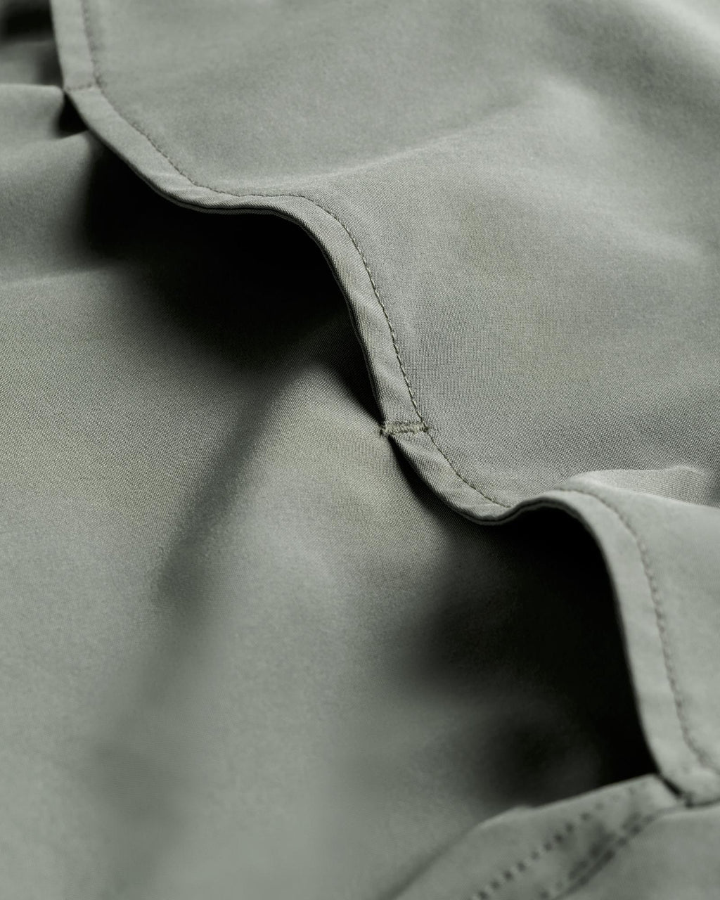 Close-up of light green fabric with visible stitching and soft folds.