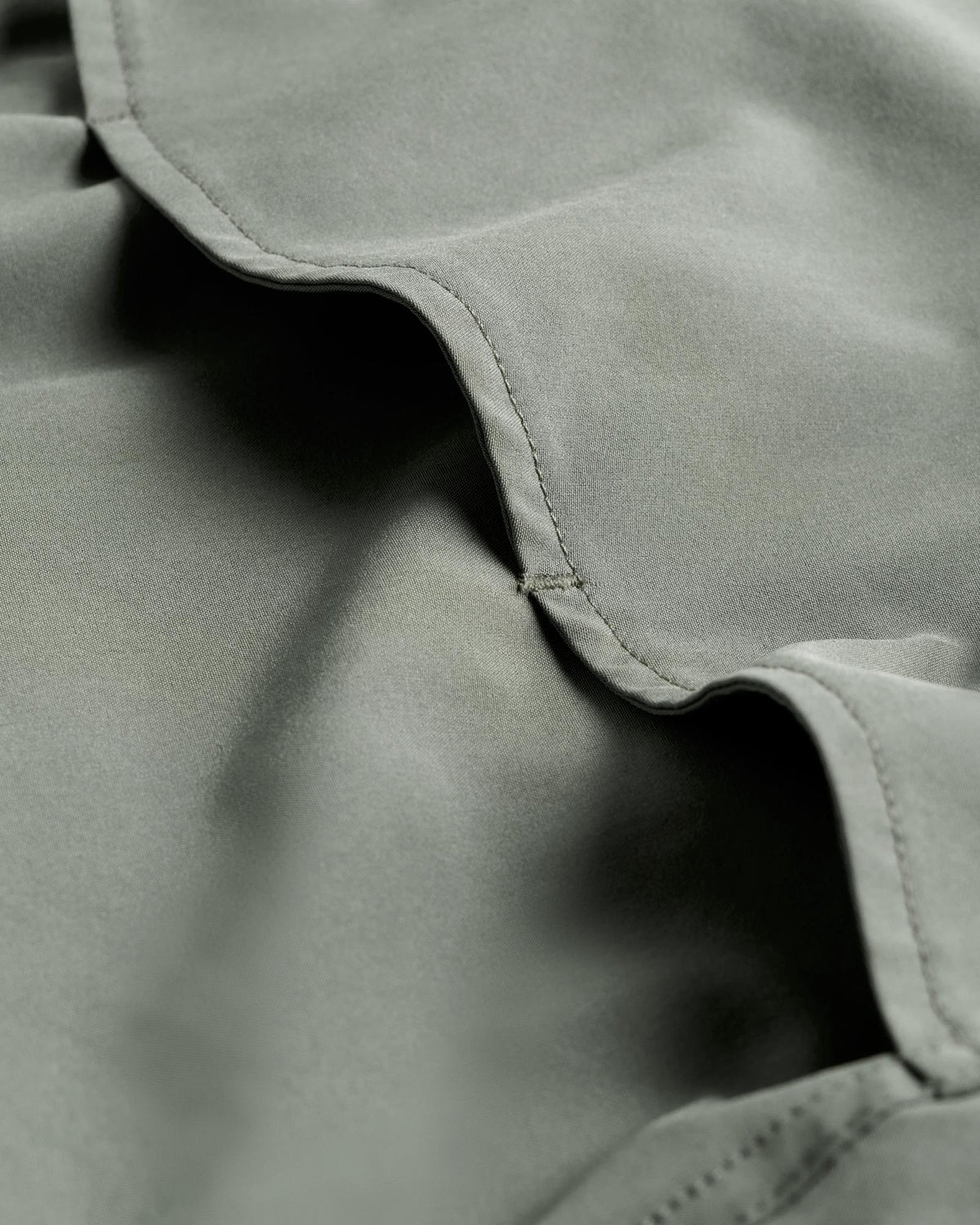 Close-up of light green fabric with visible stitching and soft folds.