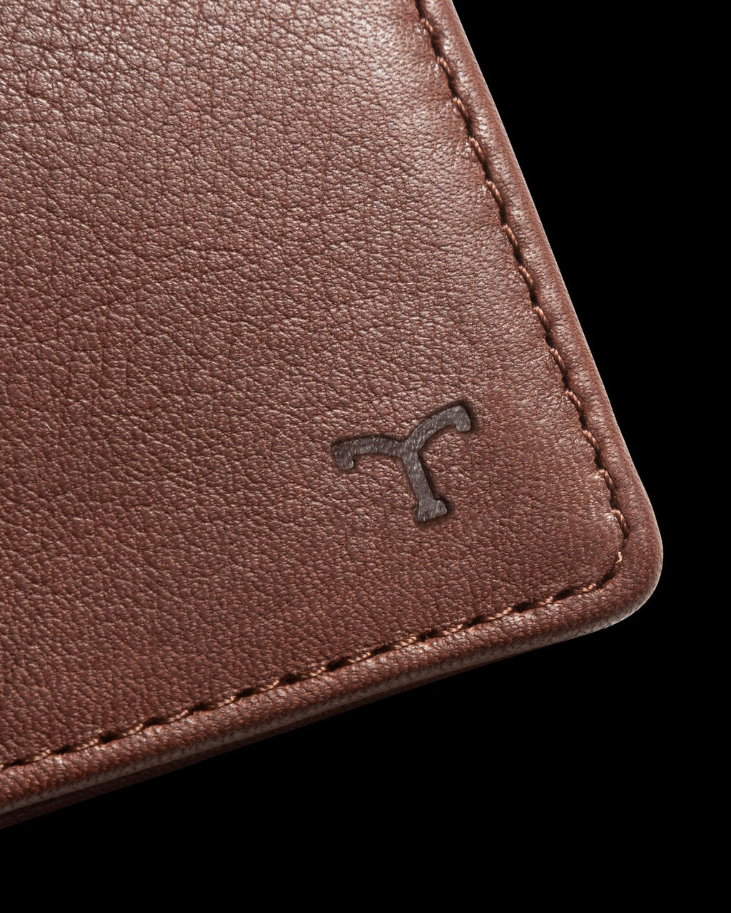 Close-up of a brown leather material with visible stitching and a small embossed logo in the corner.