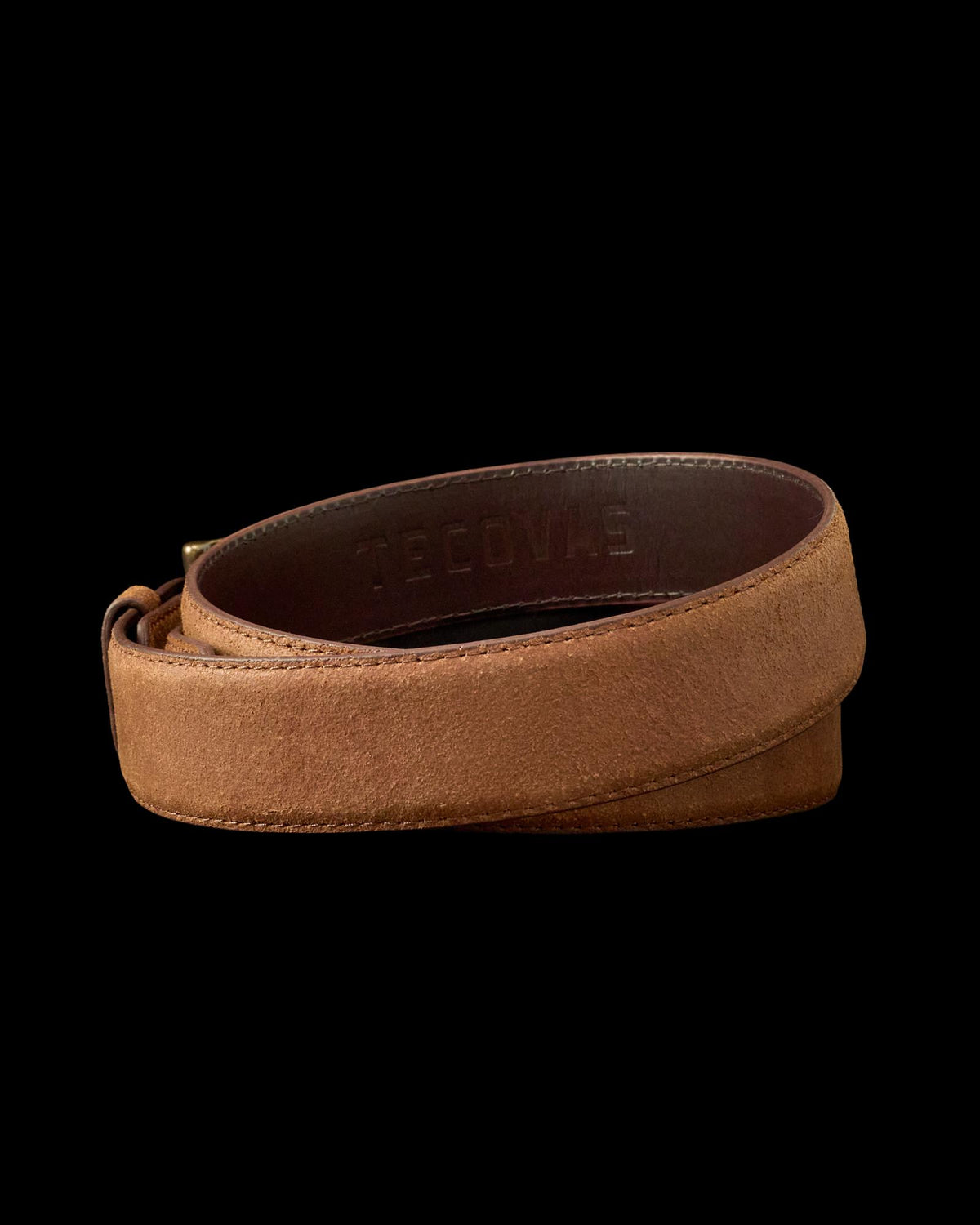 A brown leather belt with a suede finish, coiled and showing the embossed word "Tecovas" on the inner side.