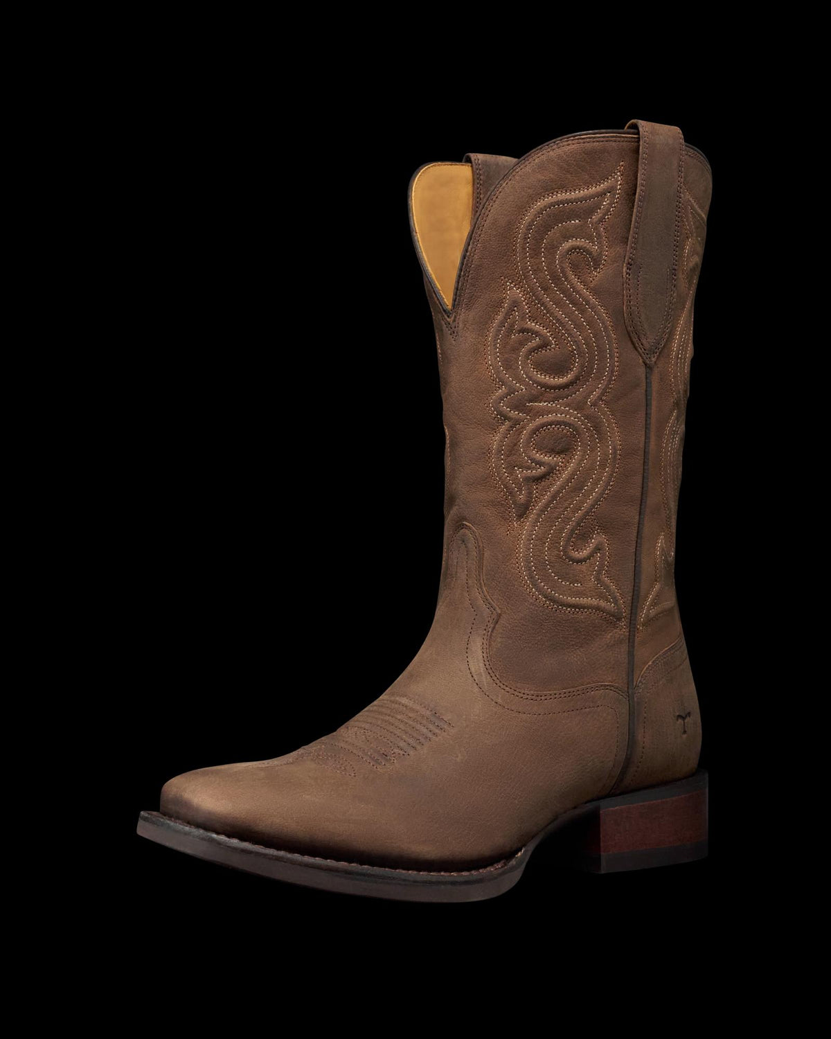 The Tess in Cafe Goat. A single brown leather cowboy boot from The Tess Goat, featuring decorative stitching, a square toe, and a low wooden heel, photographed on a plain white background.