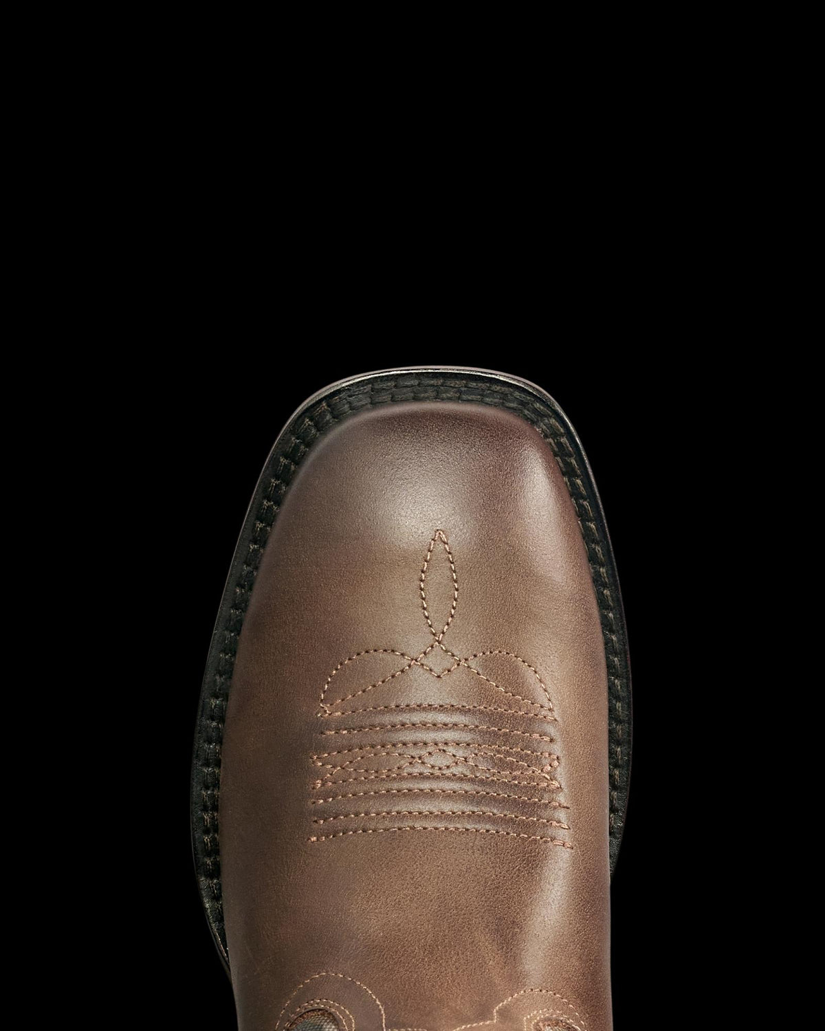 A close-up view of the toe of a brown leather boot with decorative stitching and a black sole, photographed from above.
