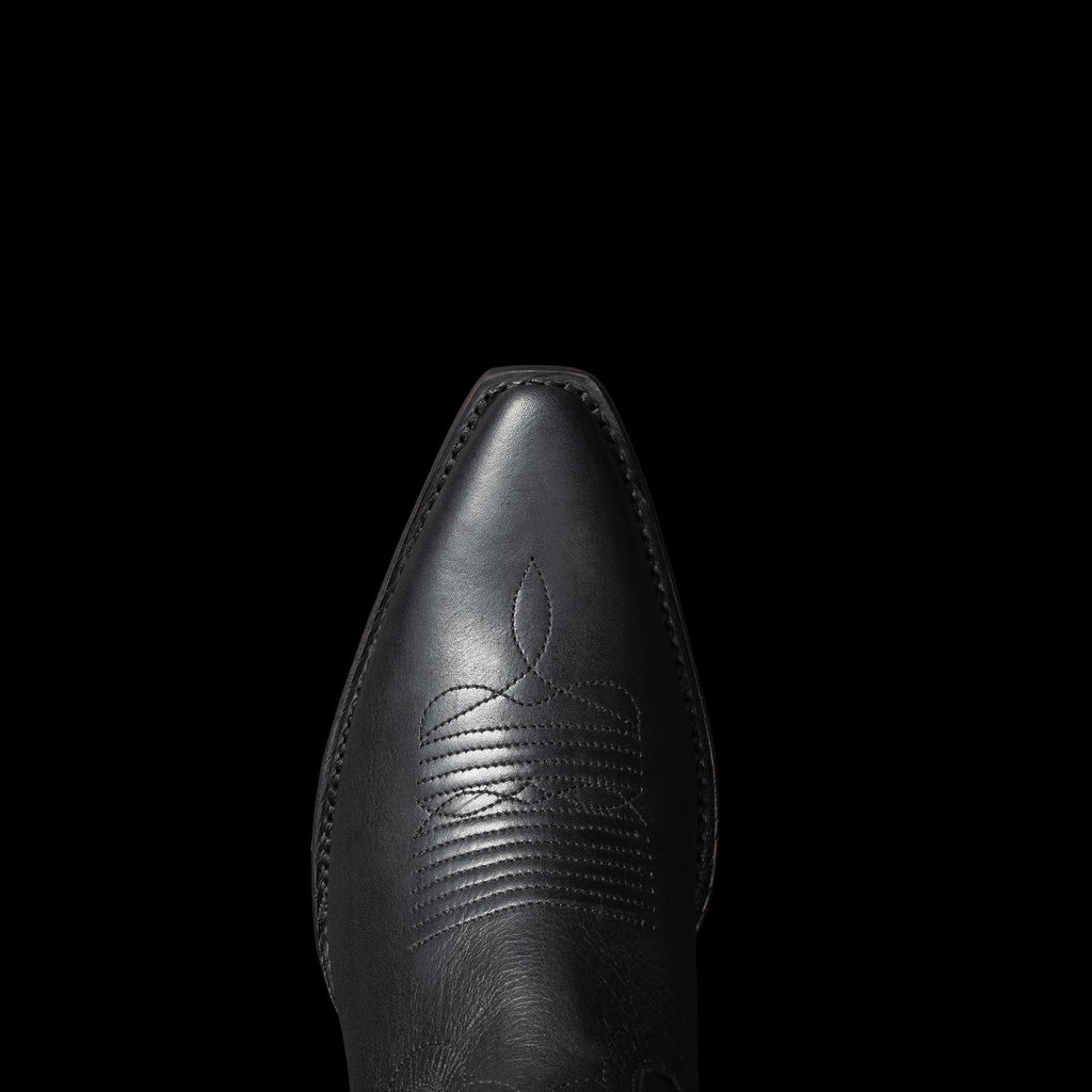 Top view of a black cowboy boot featuring intricate stitching on the toe, set against a plain black background.