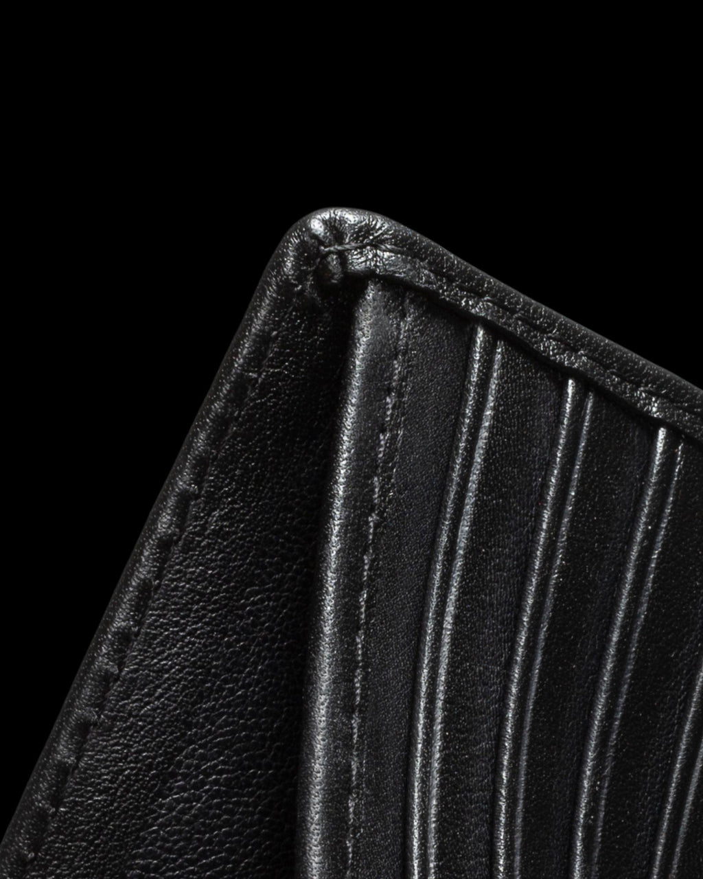 Close-up of a black leather wallet corner, showing stitching and vertical grooves, against a black background.