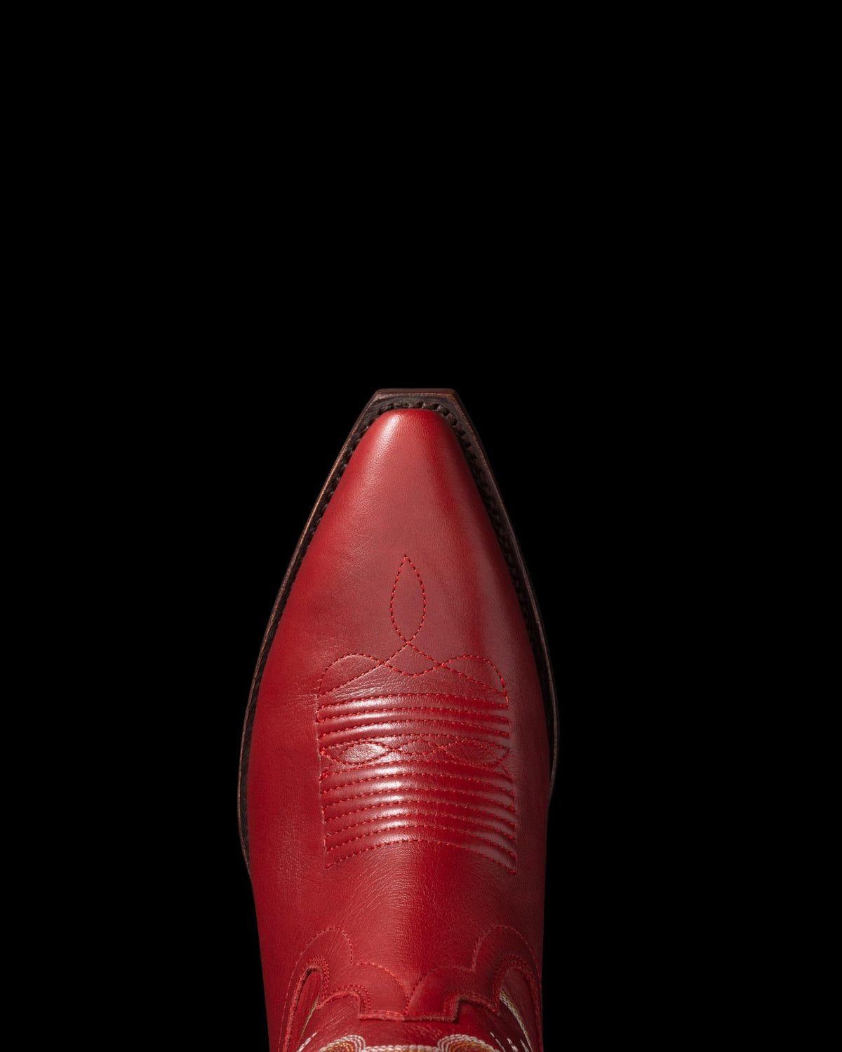 Close-up view of a red cowboy boot with intricate stitching, set against a black background.