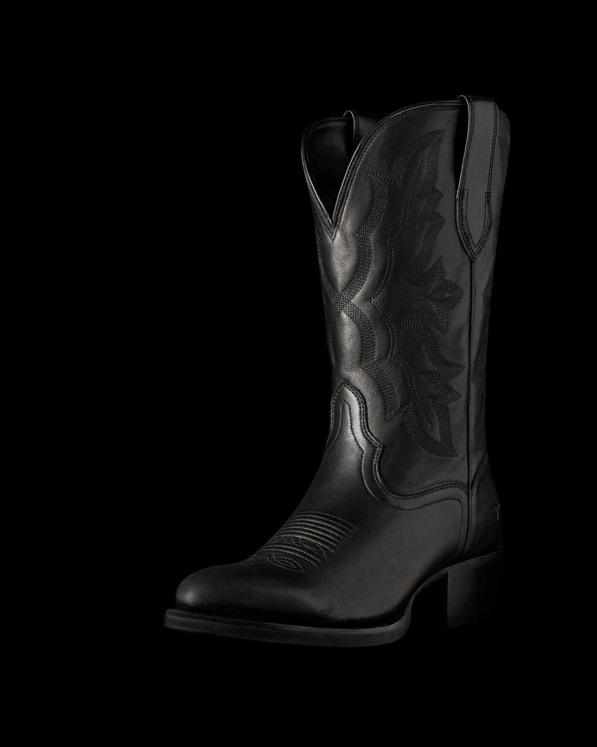 The Britt in Midnight Cowhide. Black leather cowboy boot crafted from Midnight Cowhide, featuring decorative stitching, a pointed toe, mid-calf height, pull tabs, and a low angled heel, displayed on a plain white background.