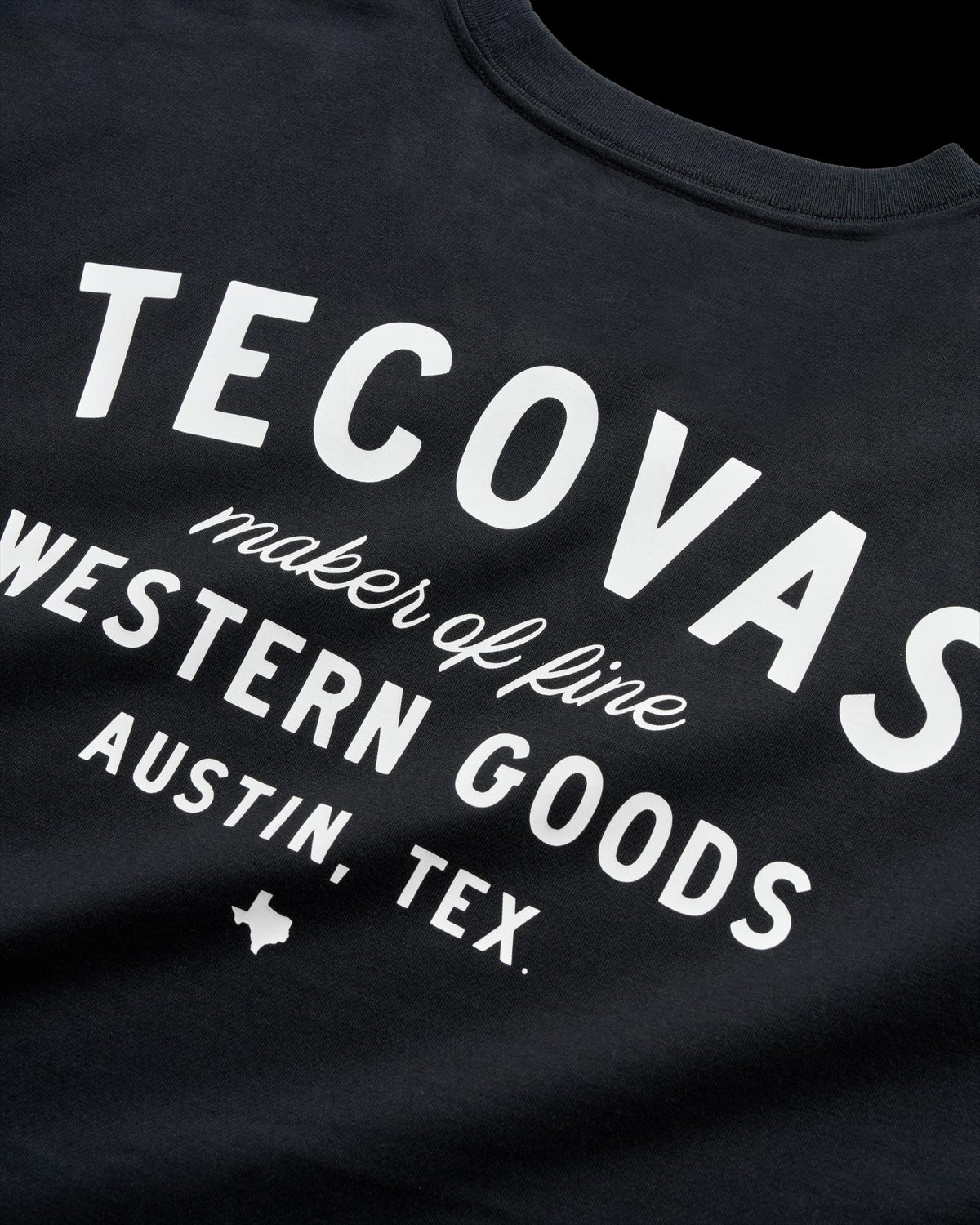 Black T-shirt with white text reading "Tecovas maker of fine Western goods Austin, Tex." and a small Texas silhouette graphic.