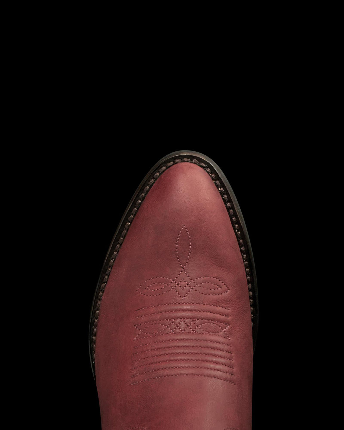 The Britt in Redwood Goat. Close-up of a maroon Redwood Goat leather cowboy boot toe with decorative stitching, shown against a plain white background.