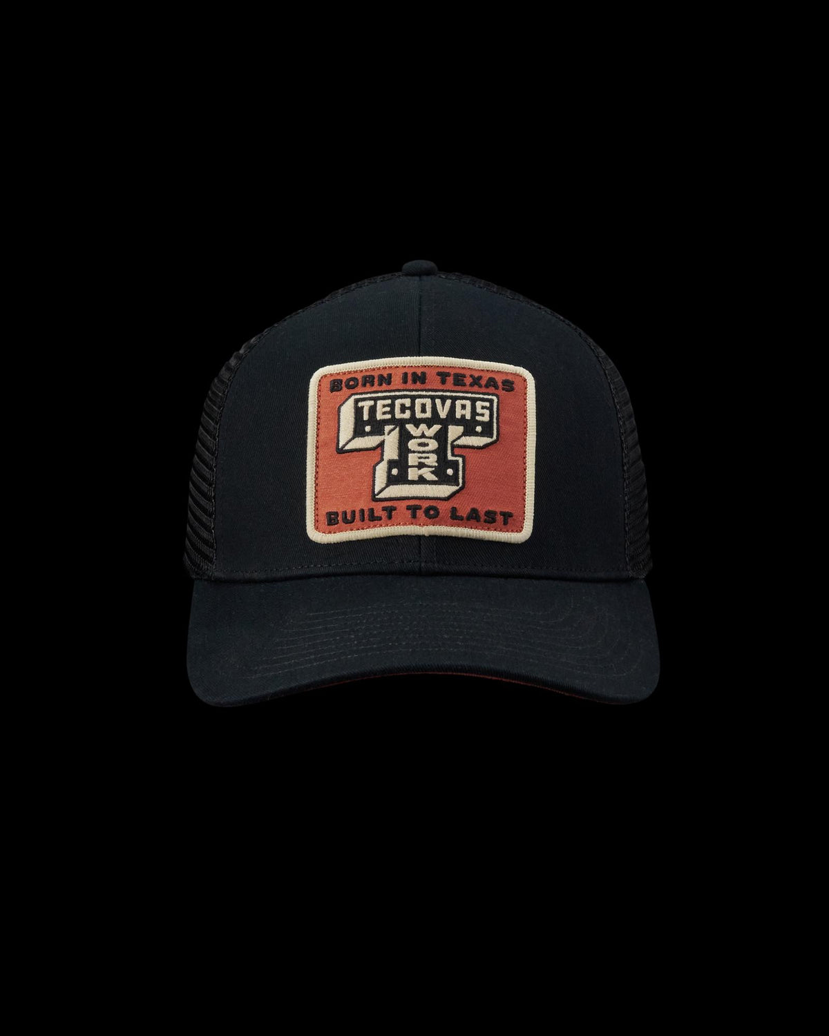 A black mesh trucker hat with a rectangular patch reading "Born in Texas Tecovas Built to Last" in tan, white, and orange colors.