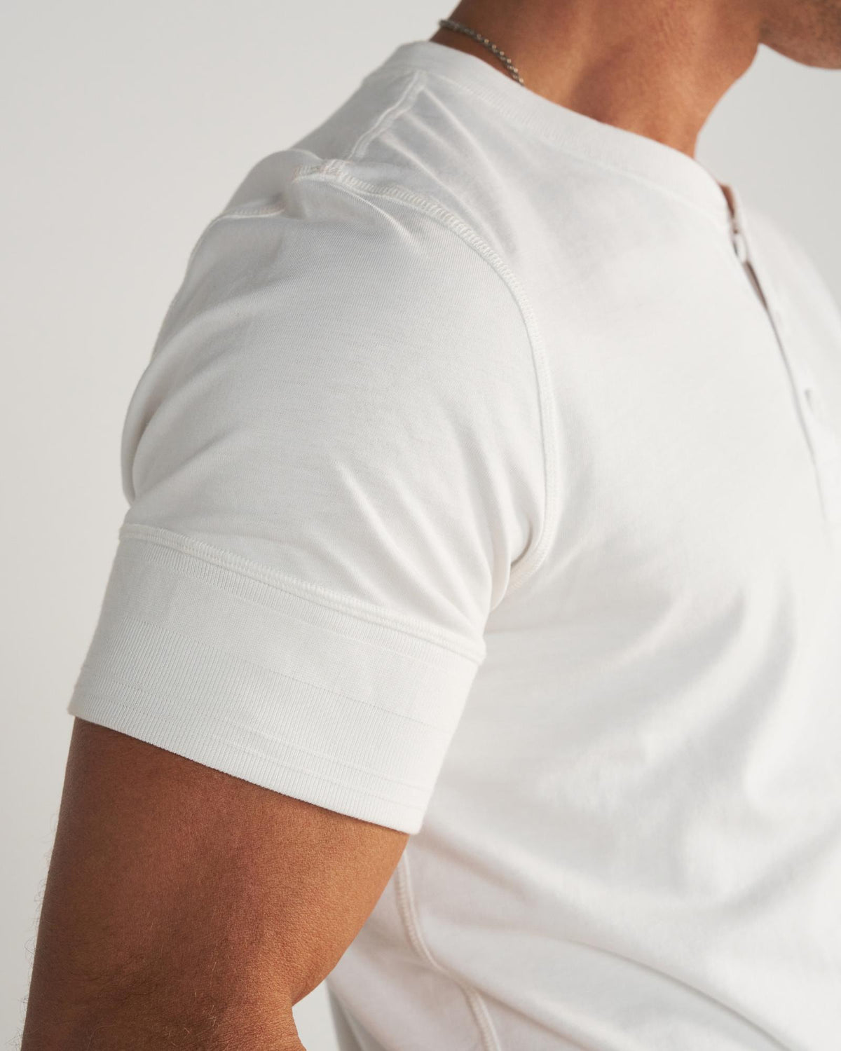 A person wearing a white short-sleeve t-shirt, blue jeans, and a cream-colored cowboy hat stands facing away from the camera against a plain background.