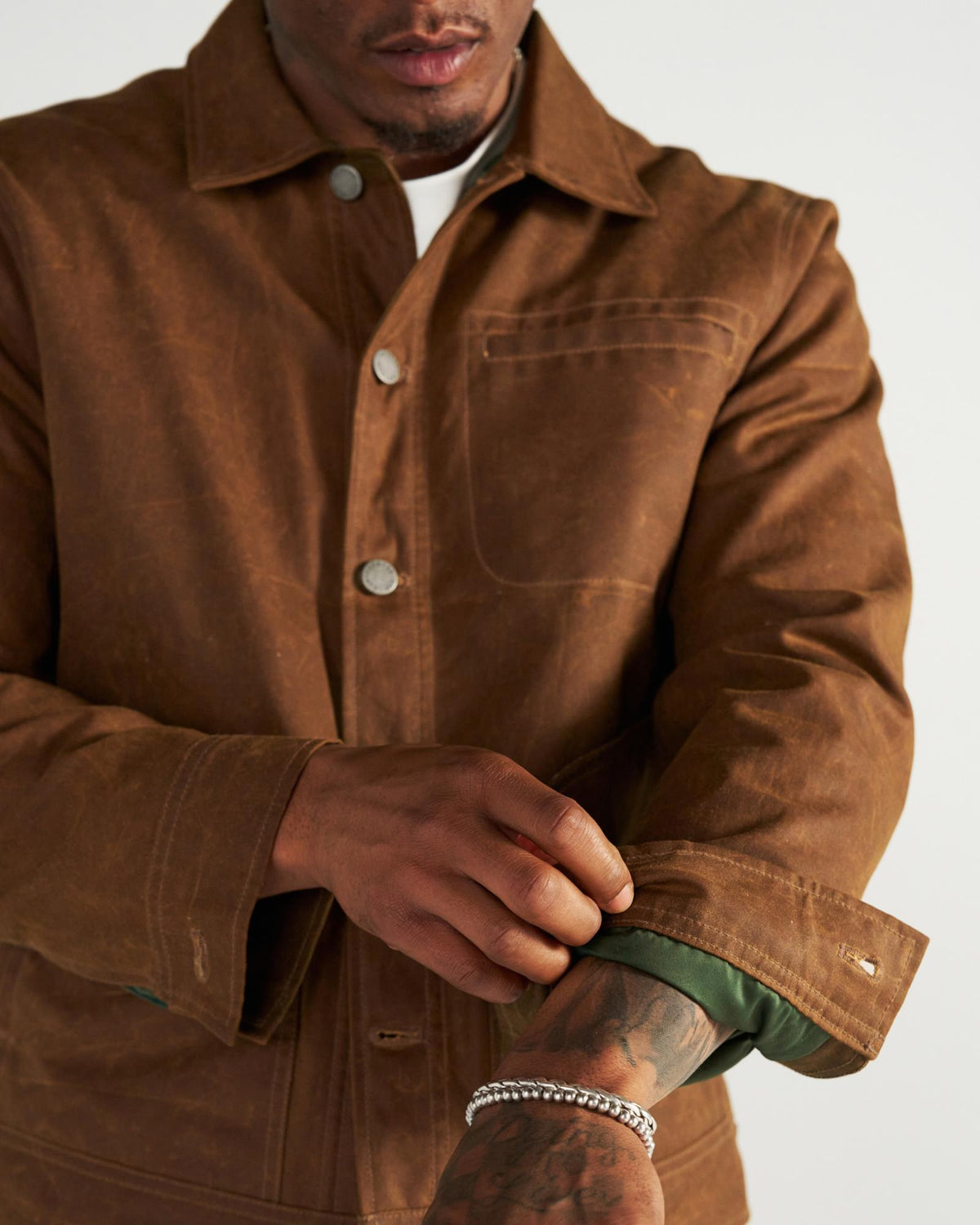 A person wearing a brown button-up jacket over a green shirt, adjusting their sleeve.