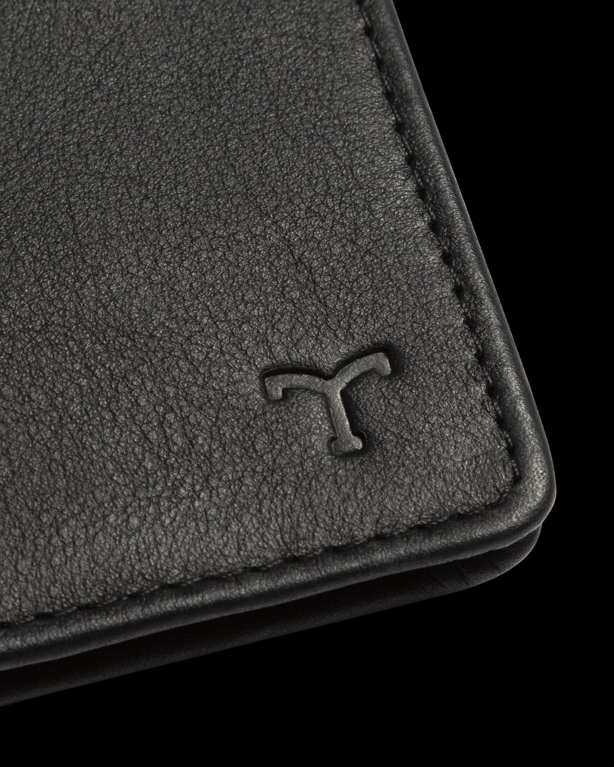 Close-up of a black leather wallet corner with a T logo embossed on the surface.