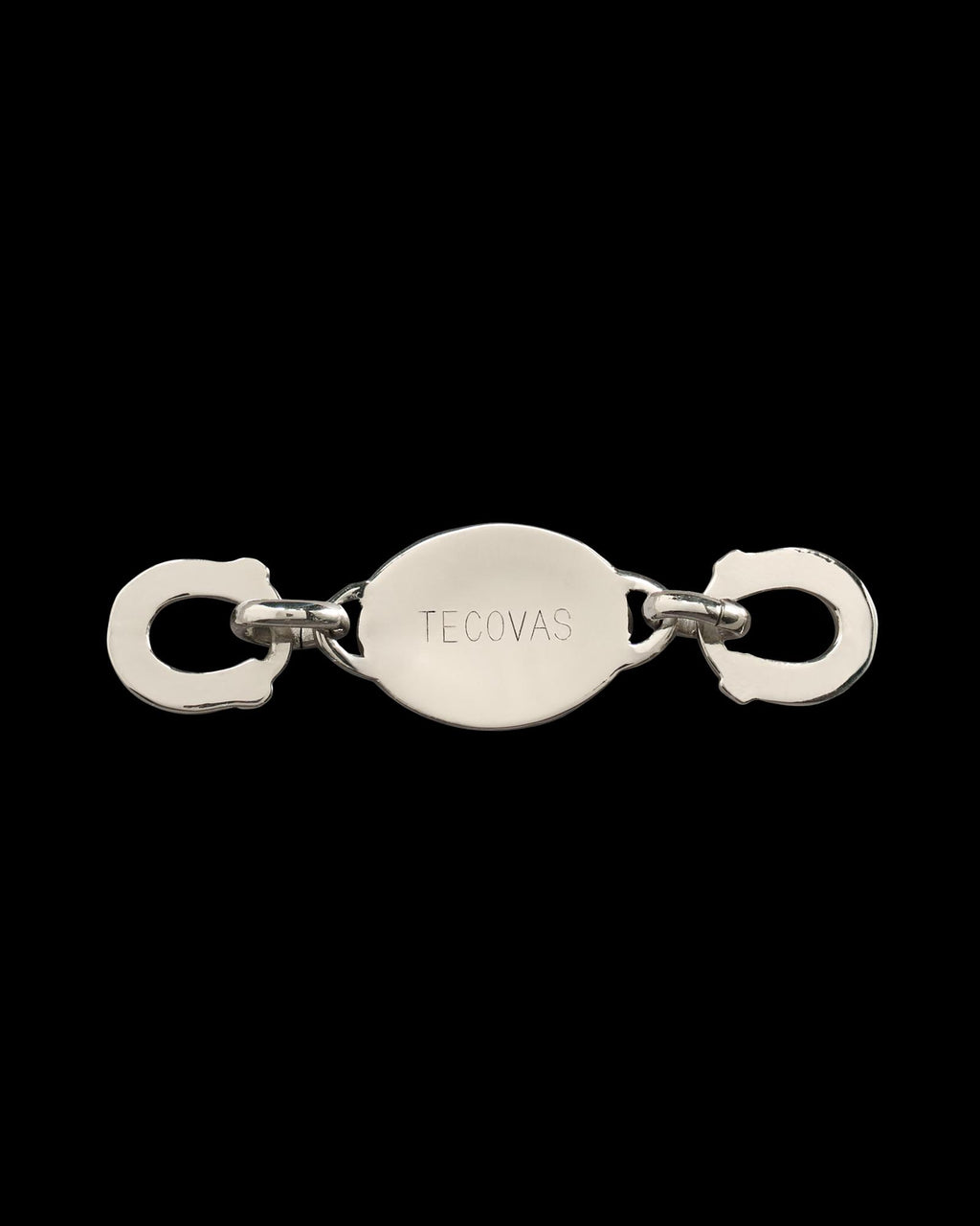 A silver metal clasp with two hooks on each end and an oval center engraved with the word "Tecovas.