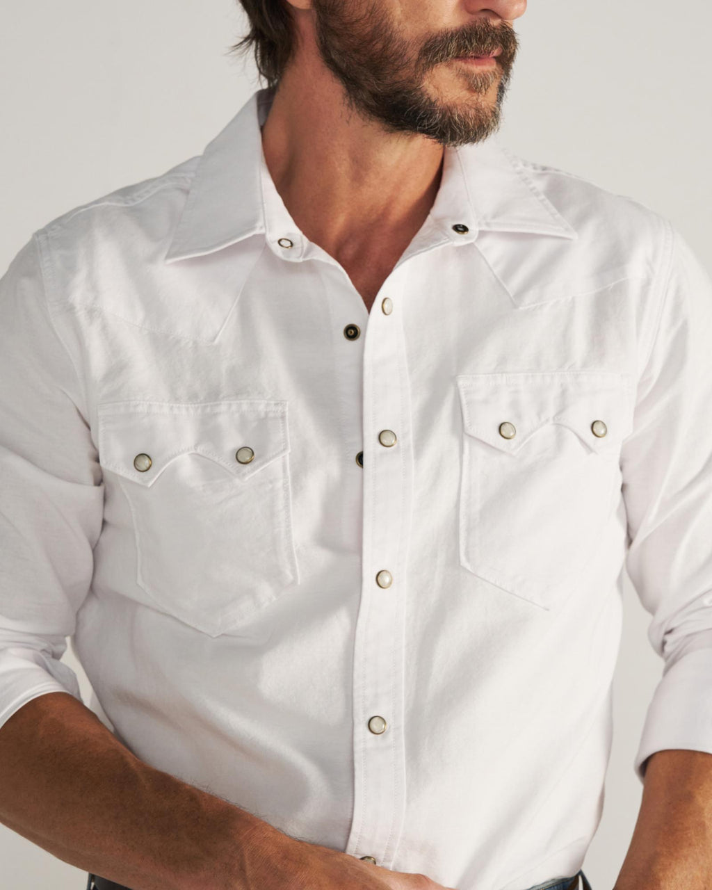 Man wearing a white long-sleeve button-up shirt with two front pockets, standing against a plain background.