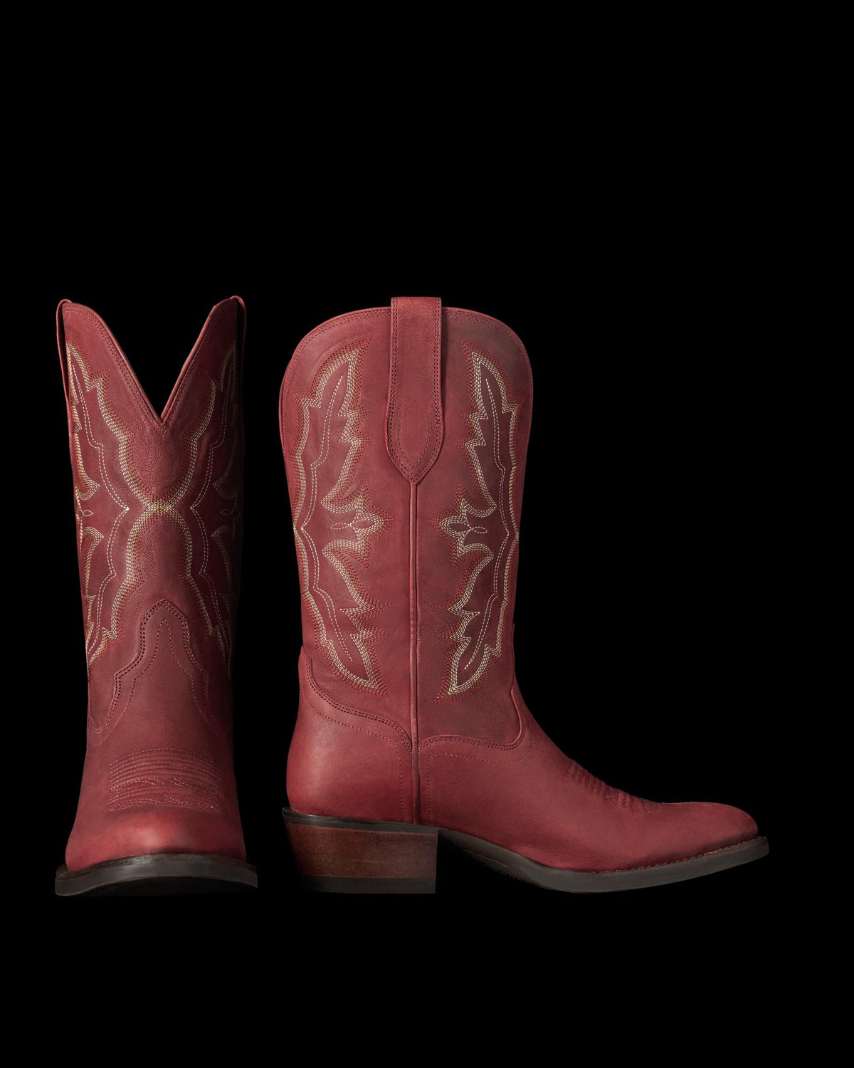 The Britt in Redwood Goat. Pair of red leather Redwood Goat cowboy boots with decorative stitching, stacked heels, and pull tabs, shown upright with one boot facing forward and the other in profile against a white background.