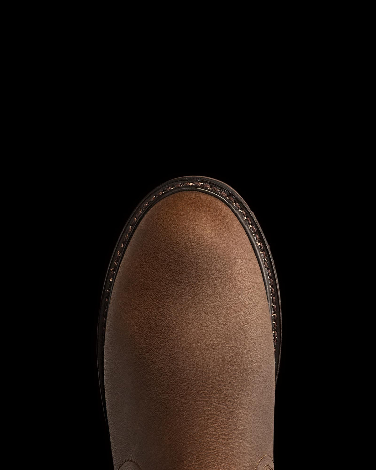 The Chelsea in Cafe Cowhide. Top view of the rounded toe of a brown leather shoe crafted from premium cowhide, with visible stitching around the edge against a plain white background.