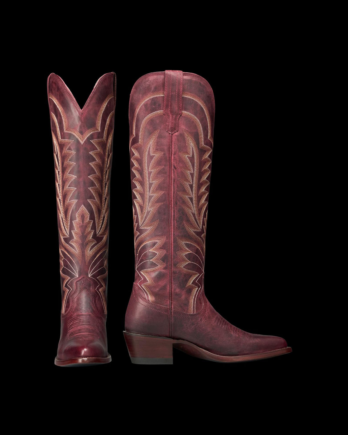 The Abby in Wine Goat. A pair of tall, burgundy leather cowboy boots from The Abby Goat, featuring decorative stitching and pointed toes, shown side by side on a white background.