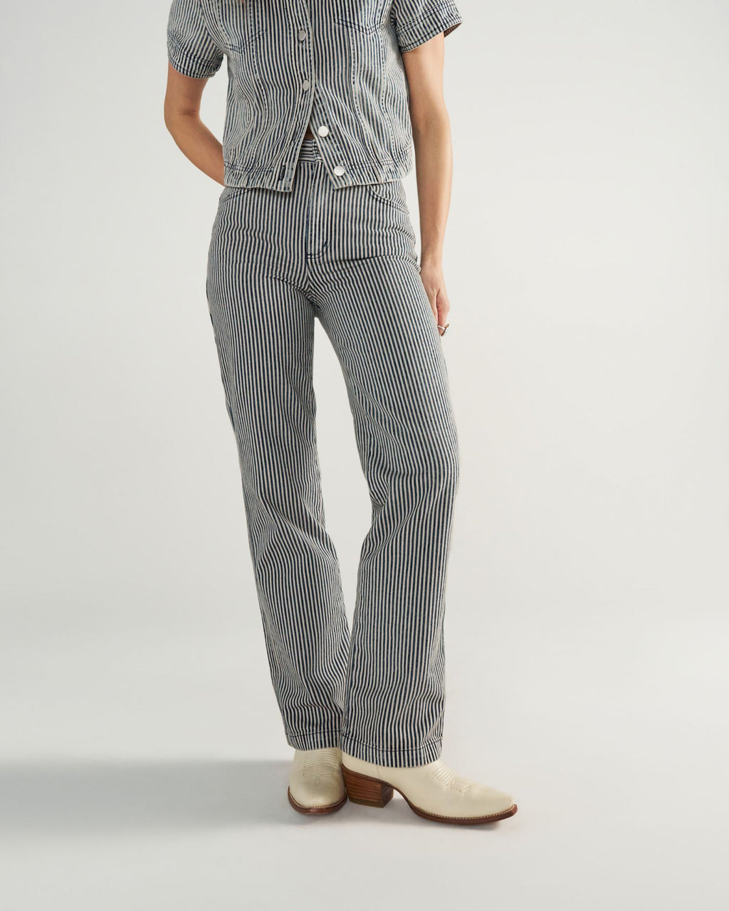 Person wearing a short-sleeve, button-up shirt and matching striped pants with white heeled shoes, standing against a plain background.