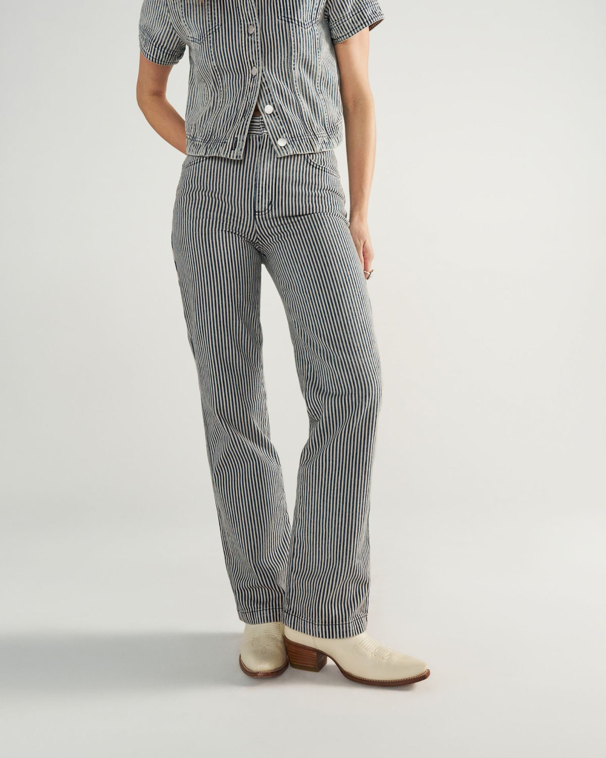 Person wearing a short-sleeve, button-up shirt and matching striped pants with white heeled shoes, standing against a plain background.