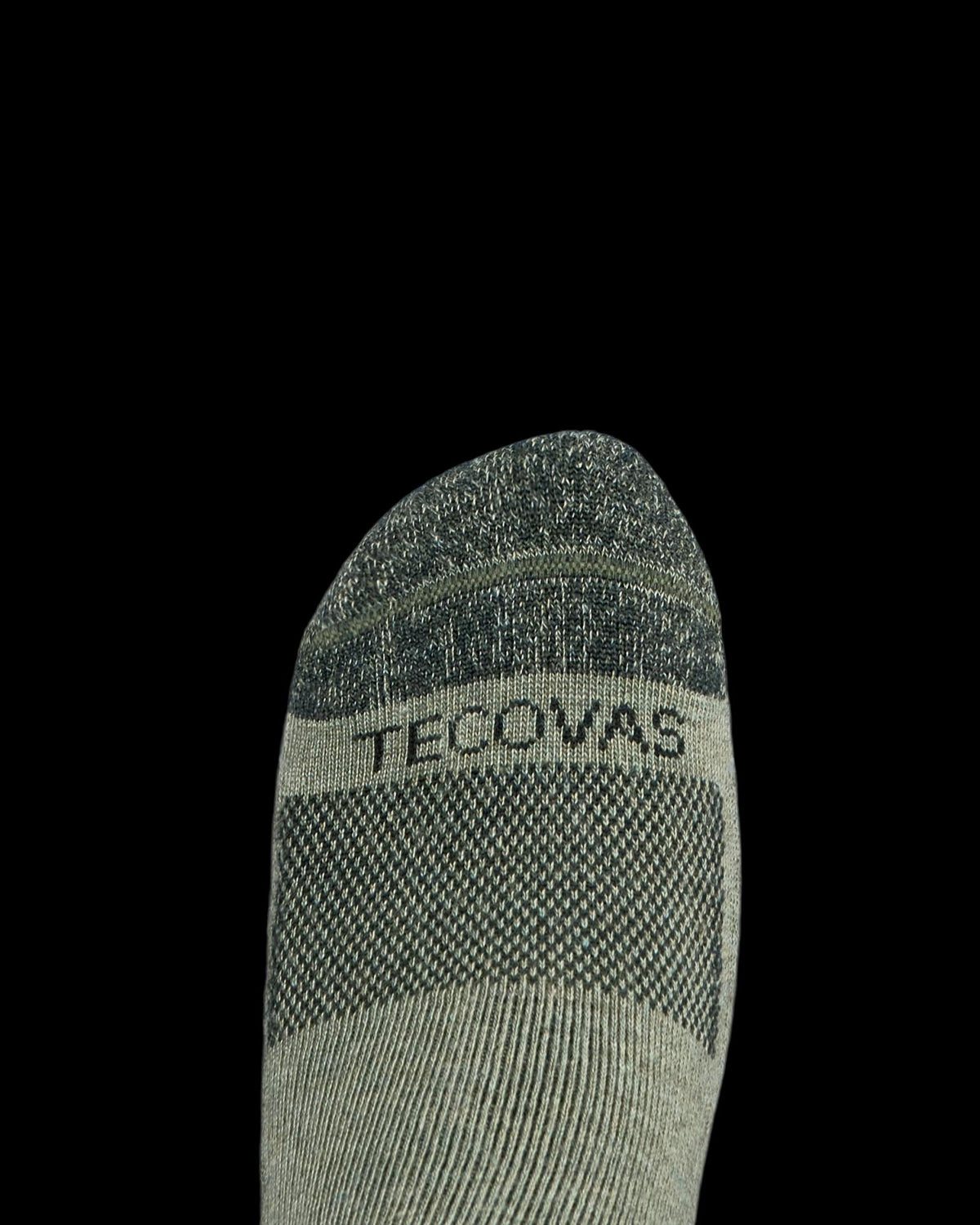 A close-up of a foot wearing a grey sock with the word "TECOVAS" printed across the top.
