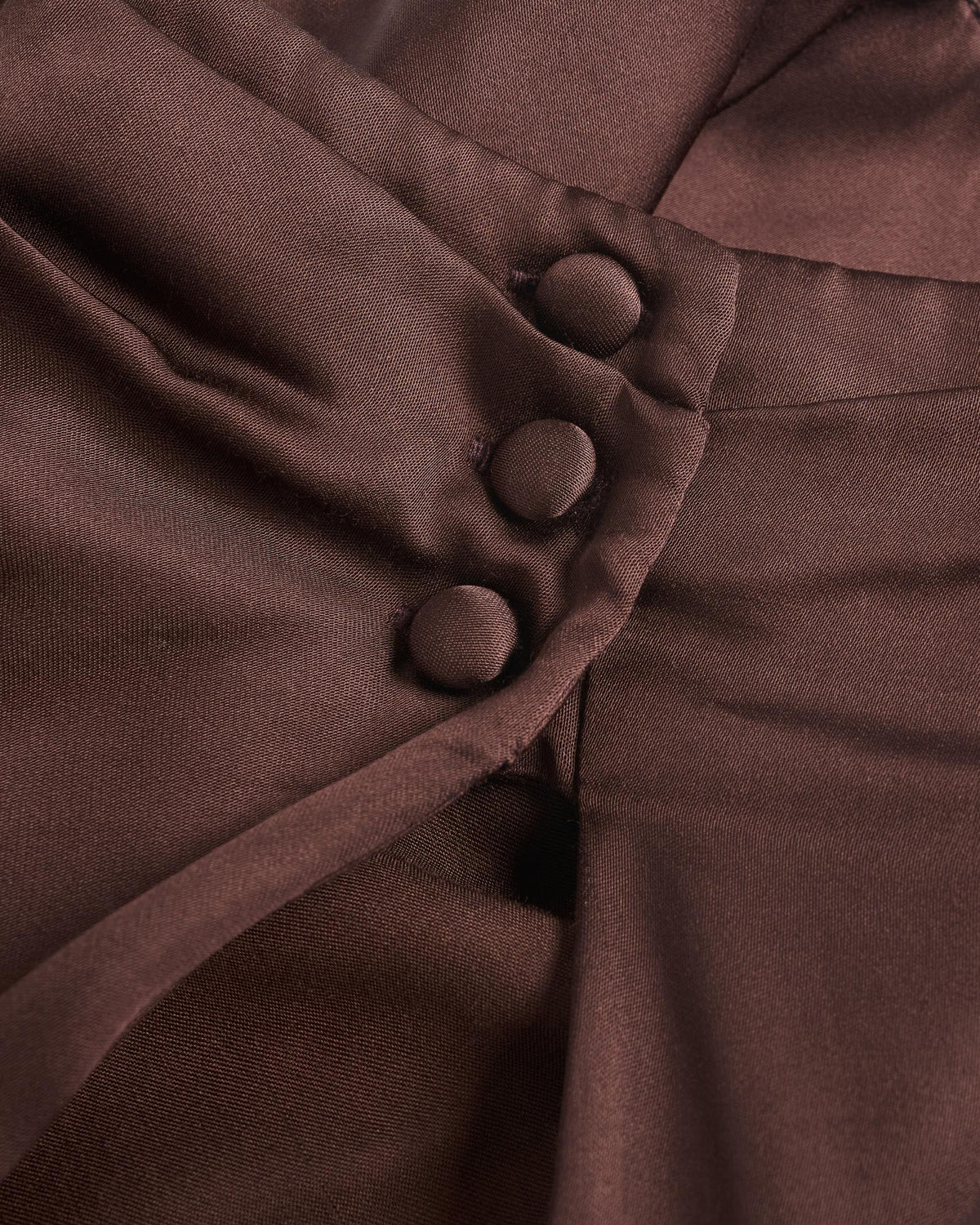 Close-up of brown fabric with three fabric-covered buttons arranged in a vertical line along a folded seam.
