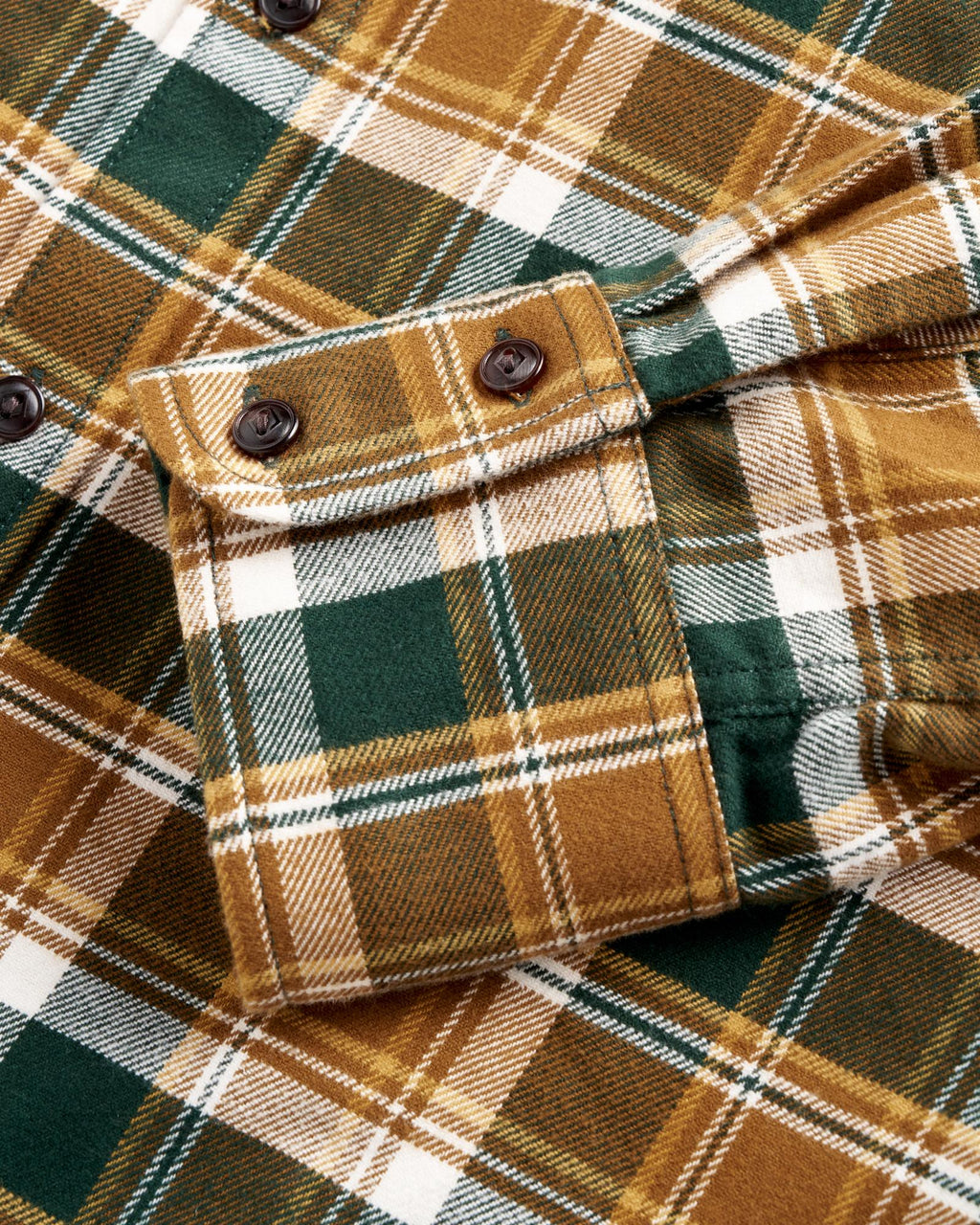Close-up of a green, brown, and white plaid flannel shirt with a folded buttoned cuff and dark buttons.
