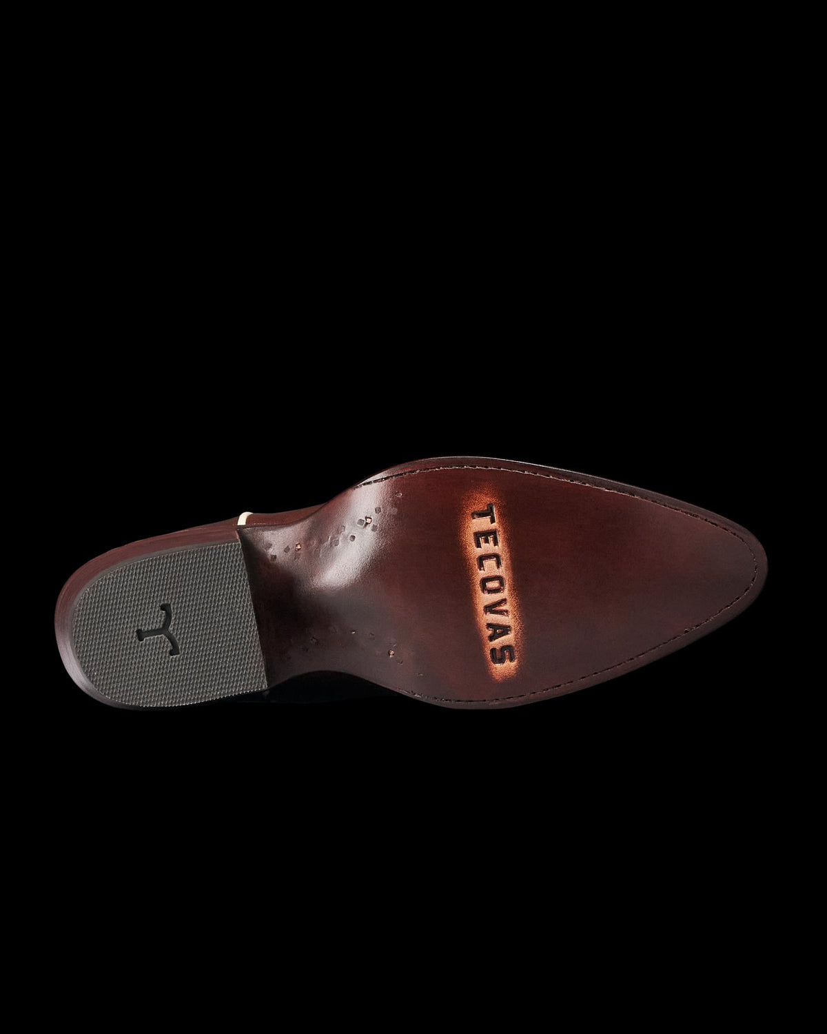 The Jolene in Truffle Cowhide. The underside of a brown leather shoe crafted from The Jolene Cowhide, with the word “Tecovas” stamped near the pointed toe and a black rubber grip on the heel.