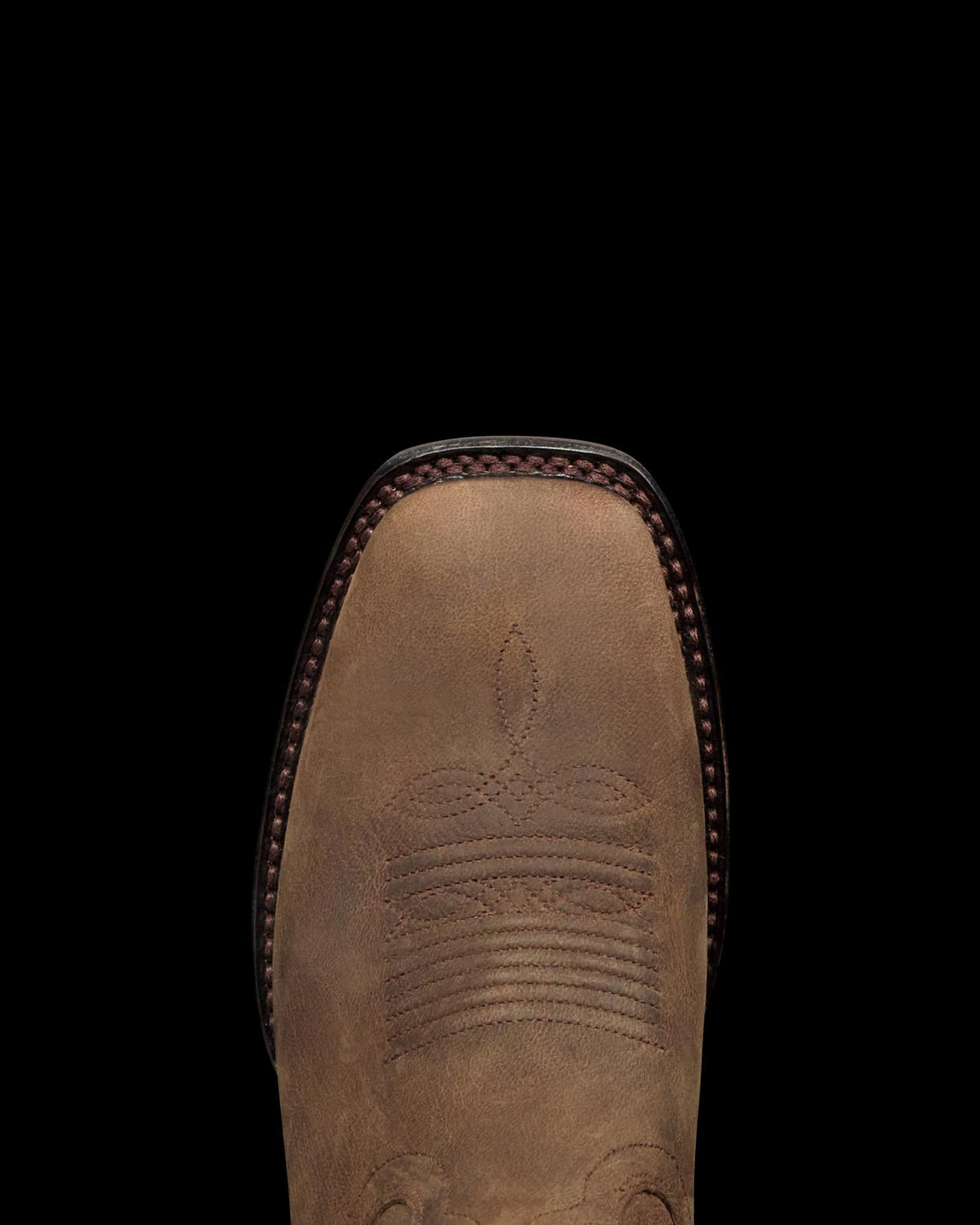 Close-up of the toe of a brown leather cowboy boot with decorative stitching and a square toe design, perfect for visiting The Tess Goat Cafe or spending time with your favorite goat.