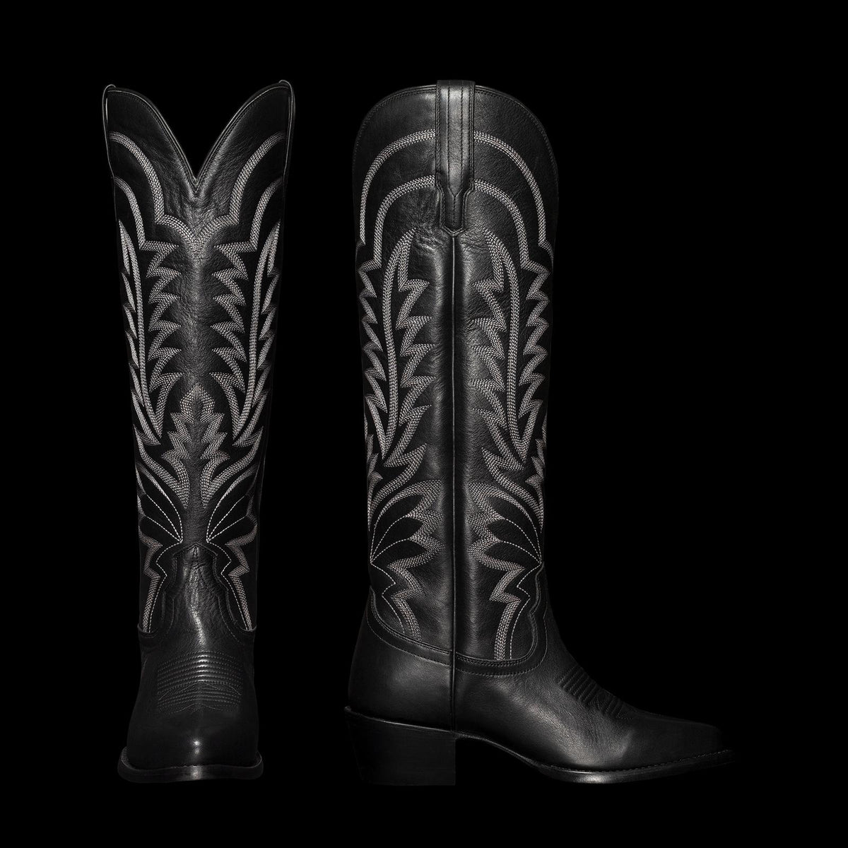 Black cowboy boots with intricate white stitching, featuring a pointed toe and a chunky heel, displayed upright and in profile.
