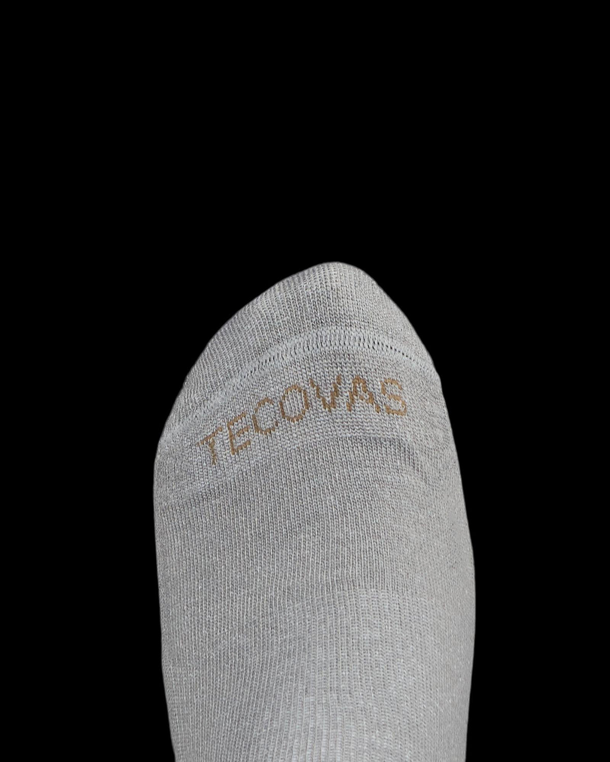 A close-up of the toe area of a light gray sock with the word "TECOVAS" stitched in tan thread on the fabric.