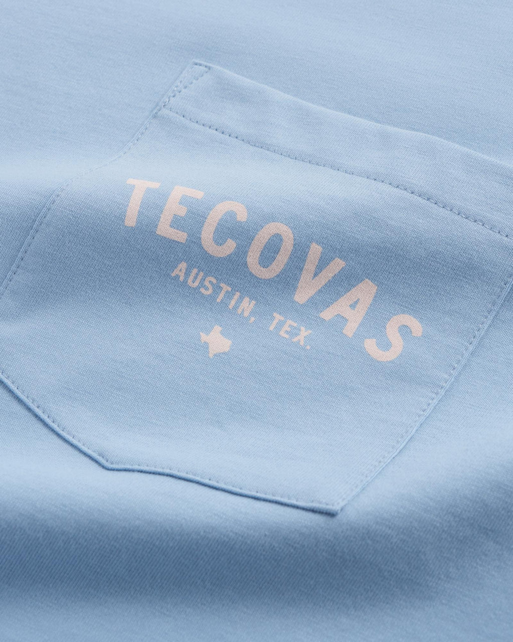 Close-up of a light blue shirt pocket with the words "TECOVAS AUSTIN, TEX." and a small Texas outline printed in white.