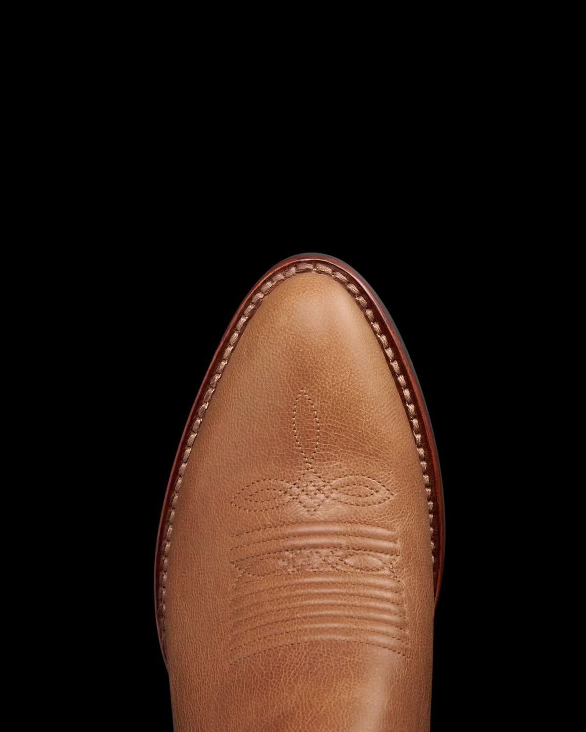 The Britt in Latte Goat. Close-up of the toe of a brown leather cowboy boot with decorative stitching, visible white welt stitching along the edge, and a subtle "Latte Goat" embossed detail accentuating its unique style.