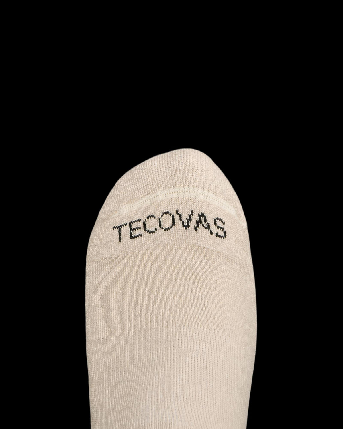 A close-up of the toe area of a beige sock with the word "TECOVAS" printed in black letters on the top.