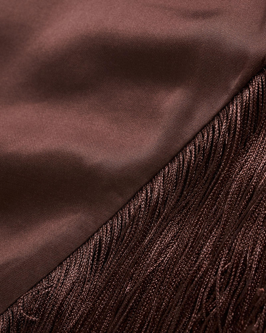 Close-up of a brown satin fabric meeting a section of matching brown fringe, showing the different textures and sheen of each material.