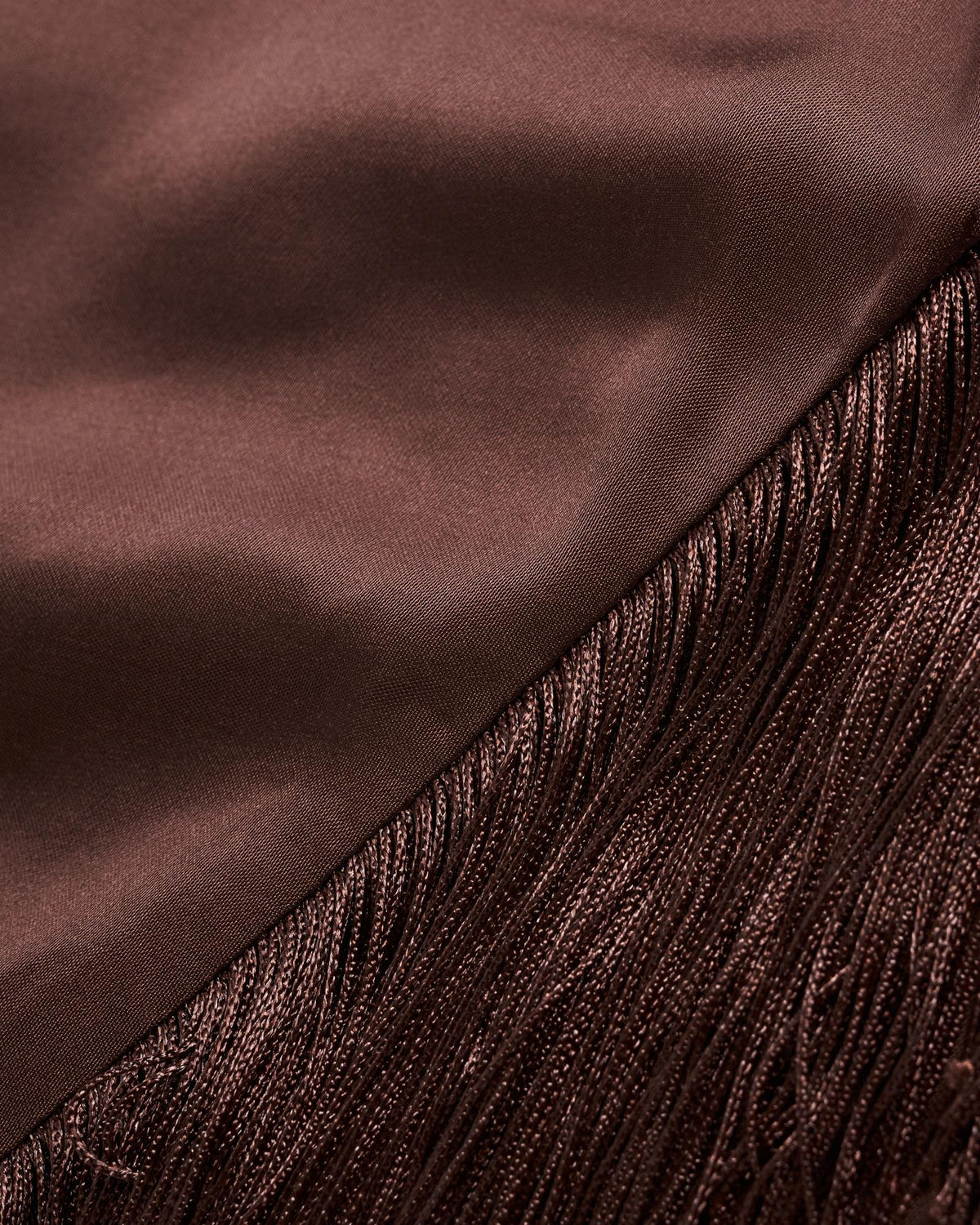 Close-up of a brown satin fabric meeting a section of matching brown fringe, showing the different textures and sheen of each material.