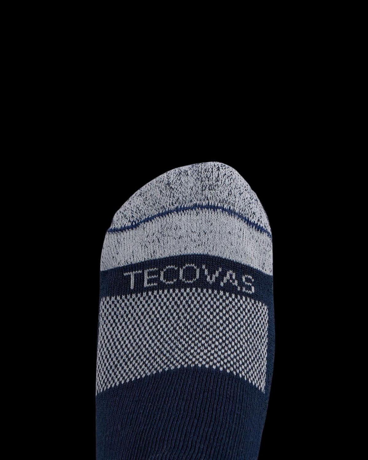 A close-up of a foot wearing a navy and gray sock with the word “Tecovas” woven across the top.